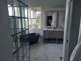 Bathroom with a black bathtub, gray vanity, marble floor, and large window.