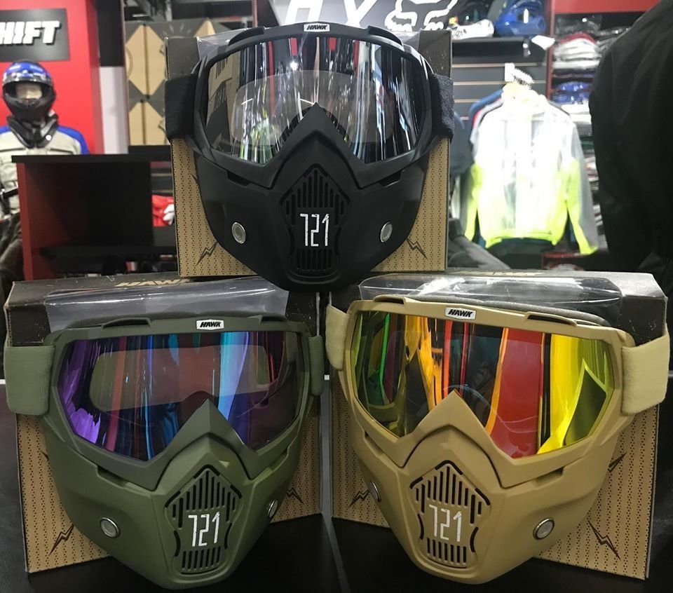 Tres gafas de motocicleta con máscaras en exhibición, de color negro, verde y tostado, con lentes reflectantes.