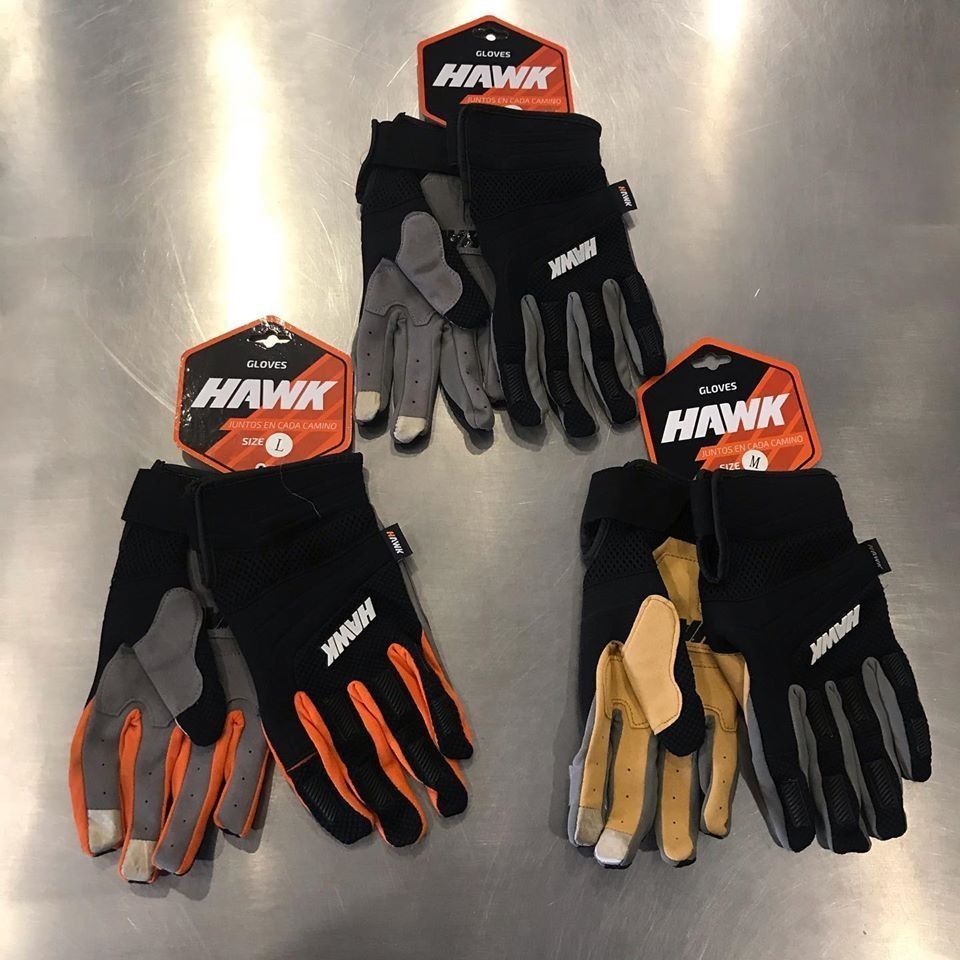 Tres pares de guantes de la marca Hawk sobre una superficie metálica, cada uno con un esquema de color diferente.