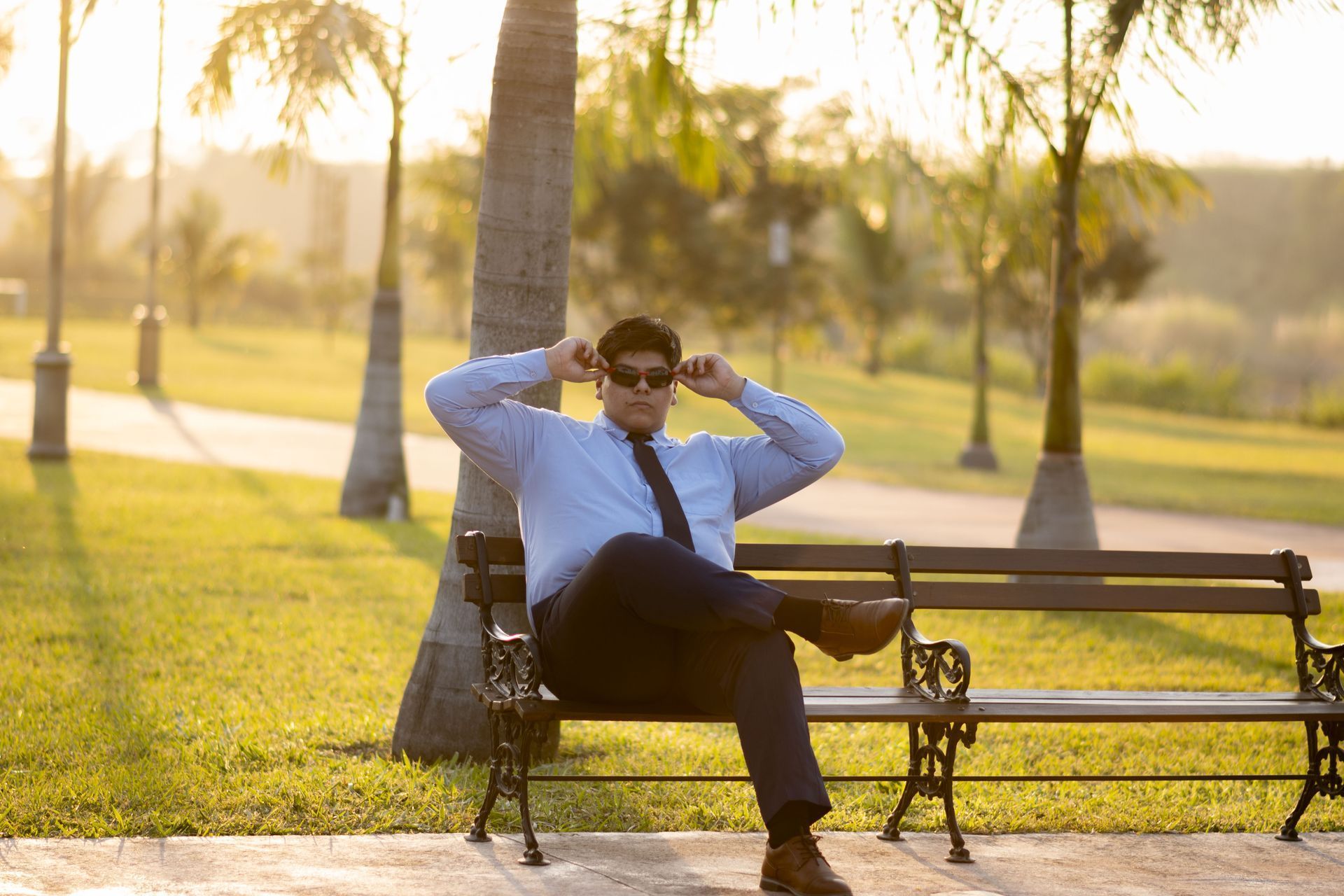 Un hombre está sentado en un banco del parque con las piernas cruzadas.