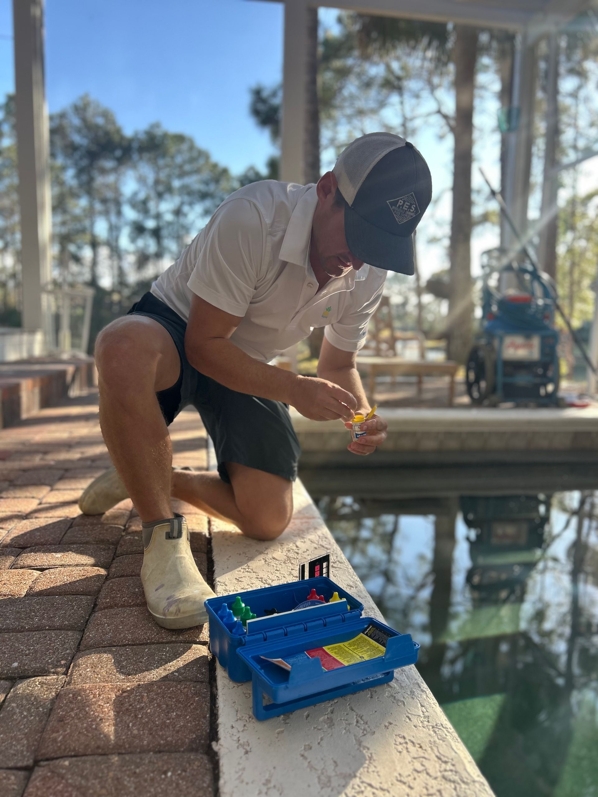 A man is kneeling on the edge of a swimming pool.
