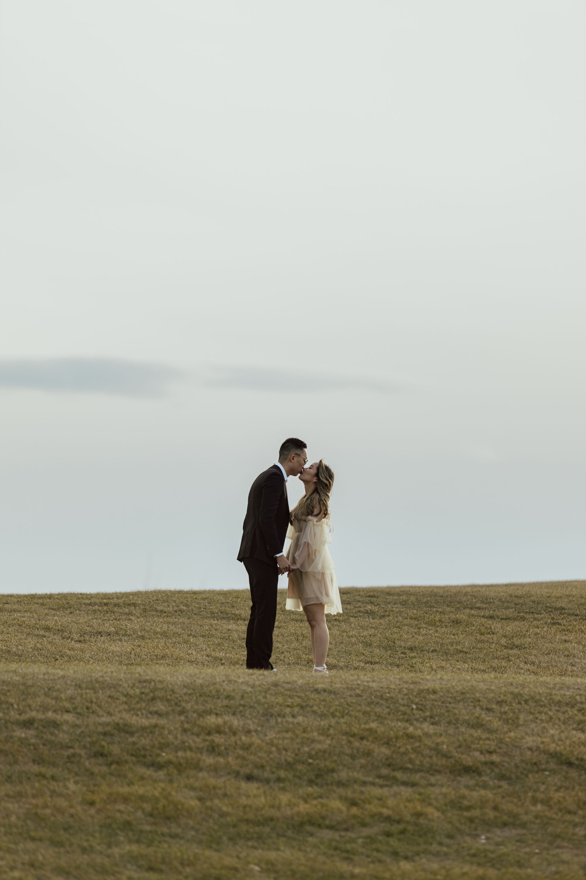 A bride and groom are kissing in a field.