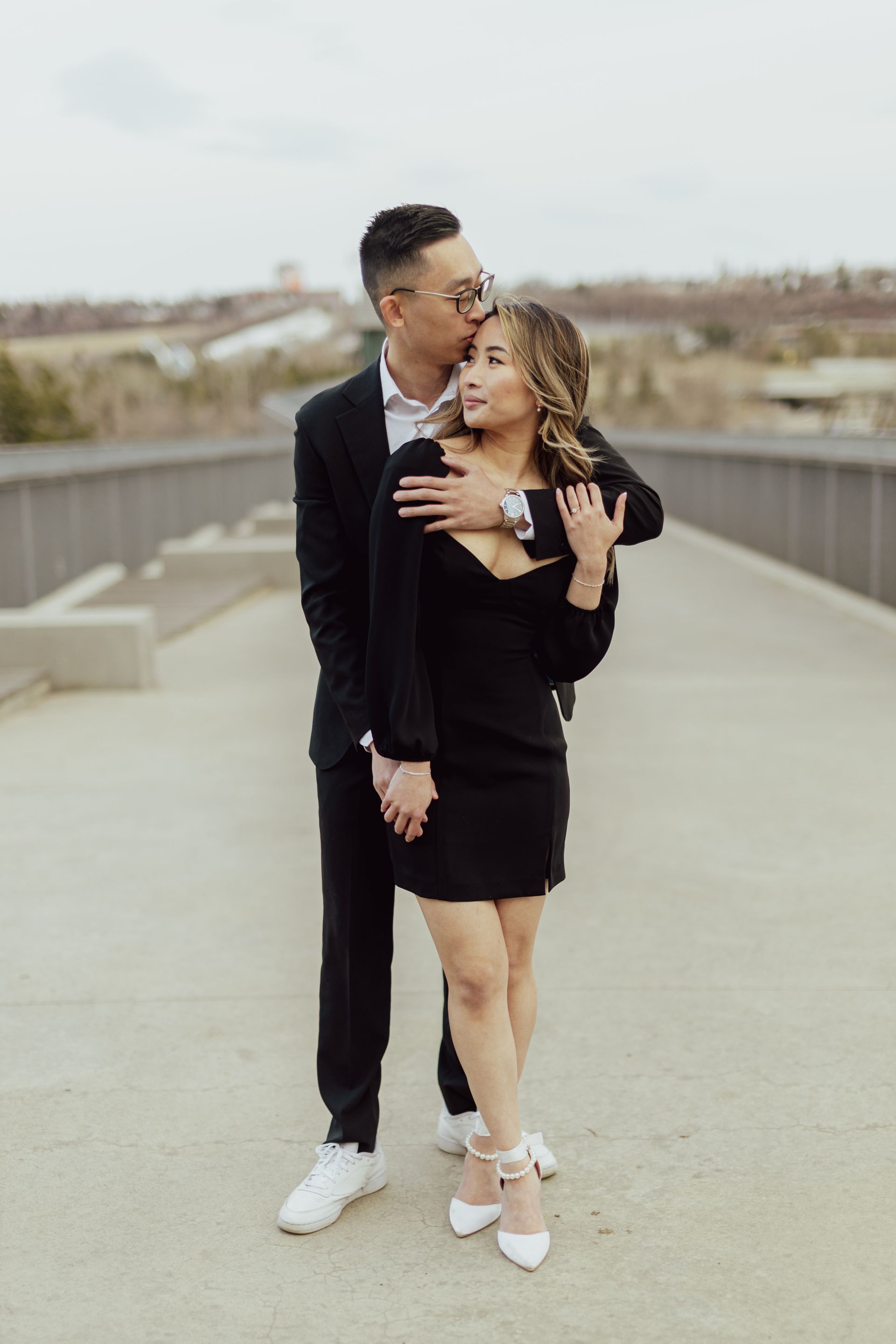 A man in a suit is kissing a woman on the forehead on a bridge.