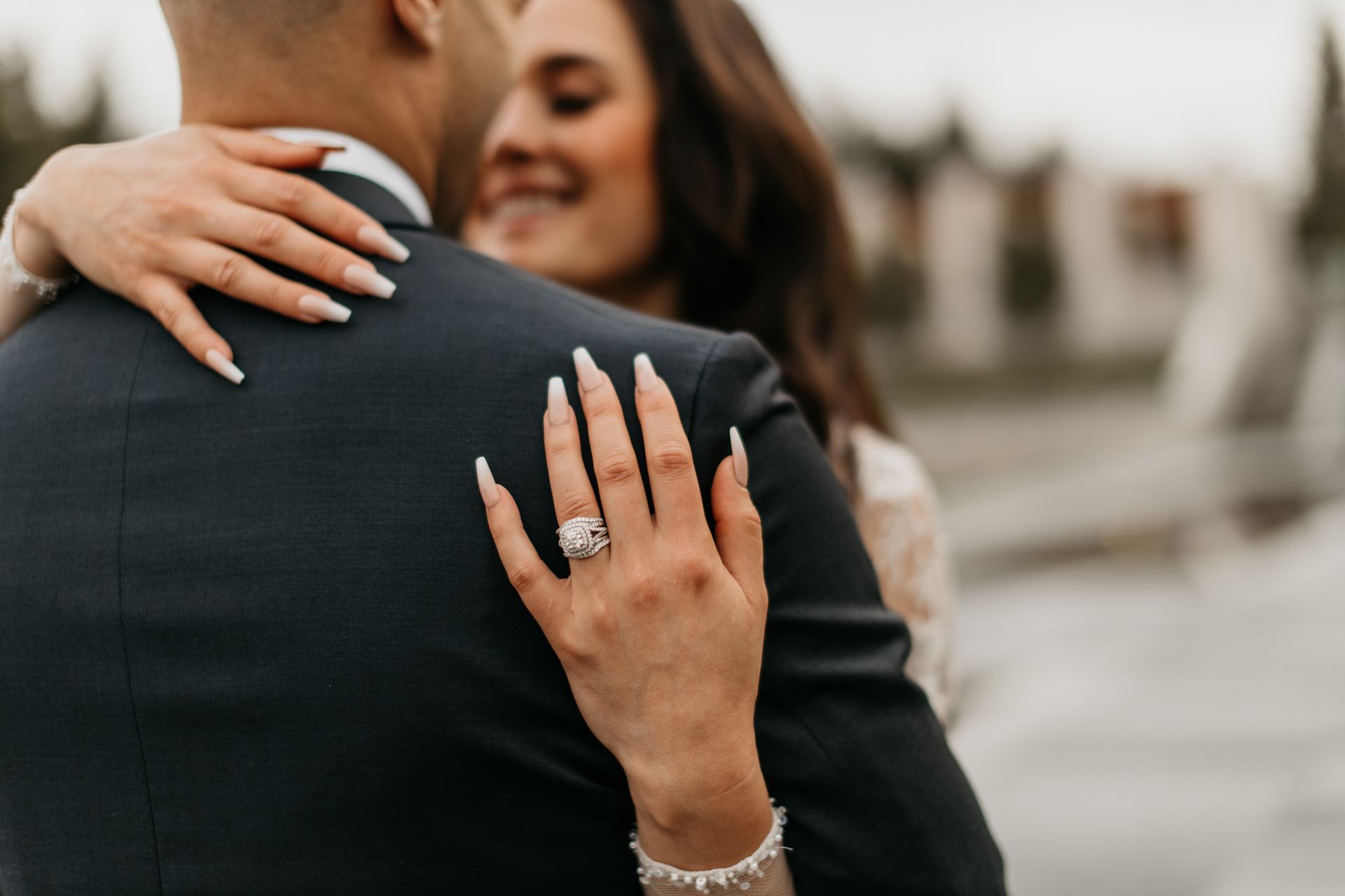 A bride and groom are hugging and the bride is wearing a diamond ring on her finger.