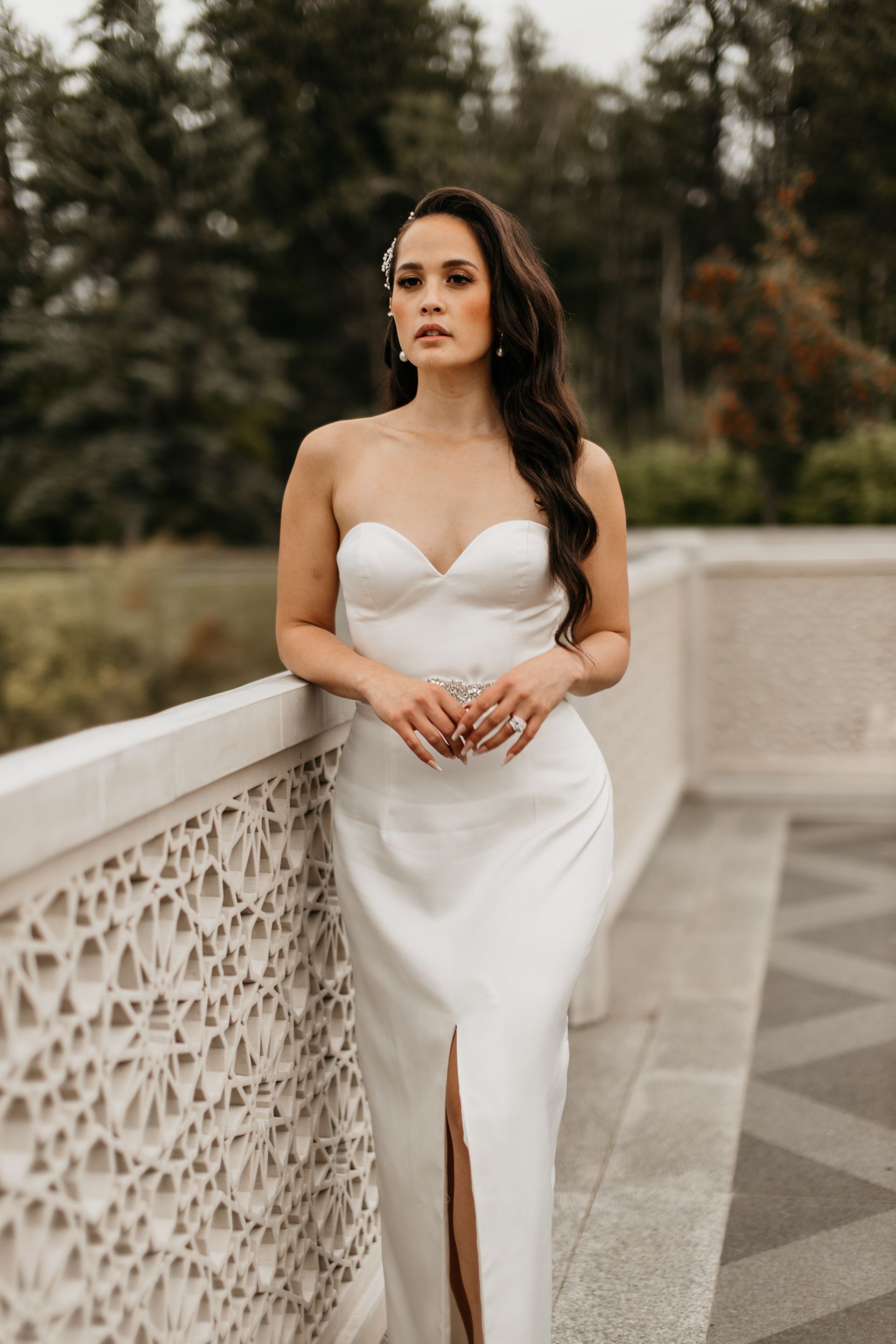 A woman in a white dress is leaning against a wall.