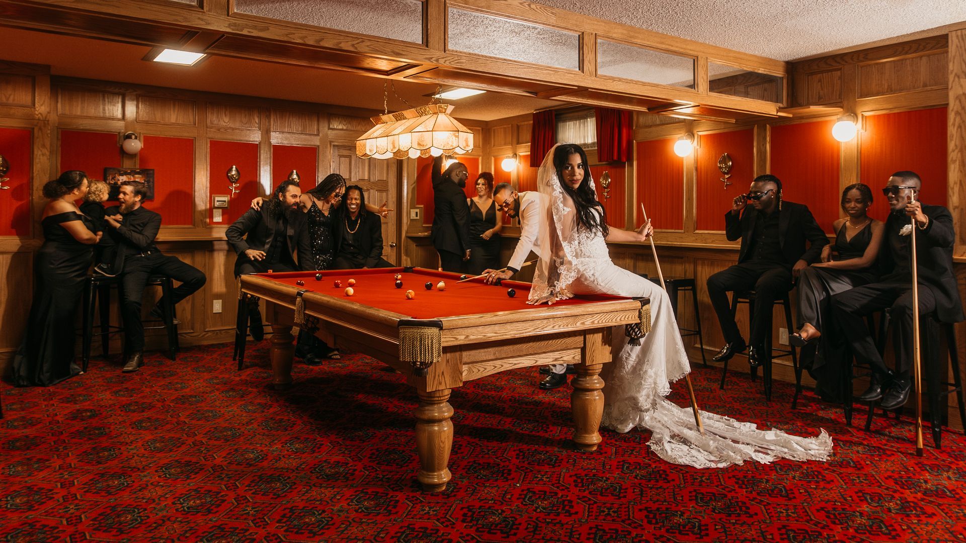 A bride in a wedding dress is sitting on a pool table surrounded by people.