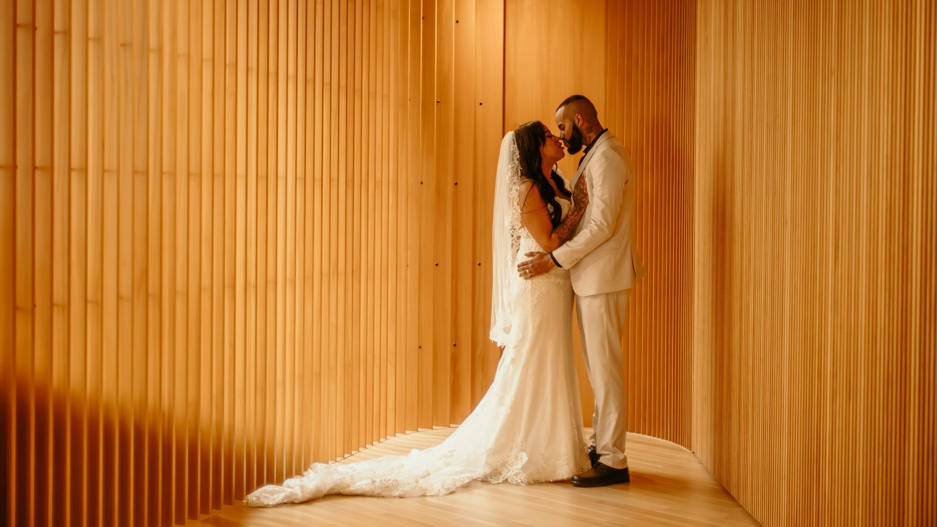 A bride and groom are kissing in front of a wooden wall.