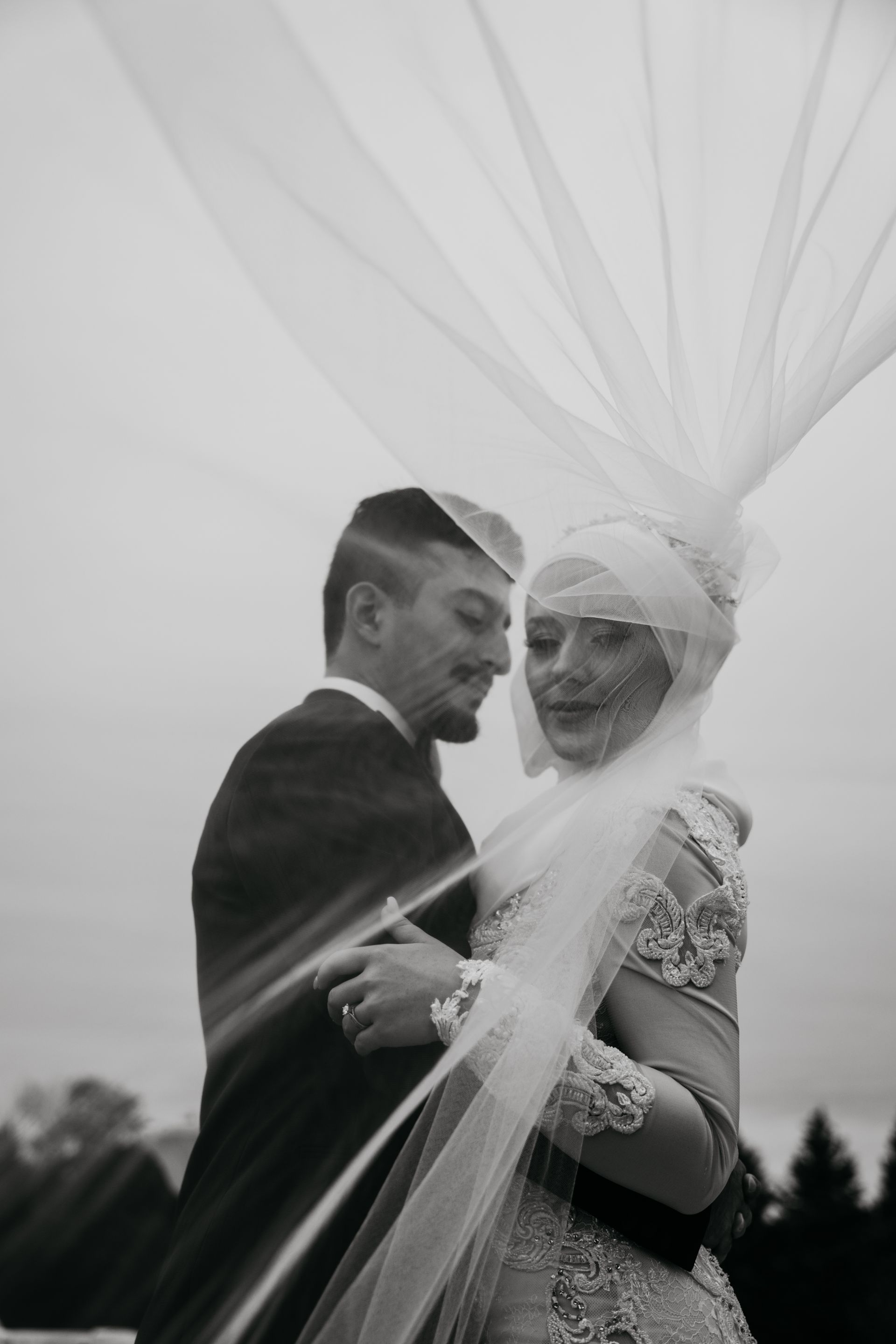 A black and white photo of a bride and groom dancing under a veil.