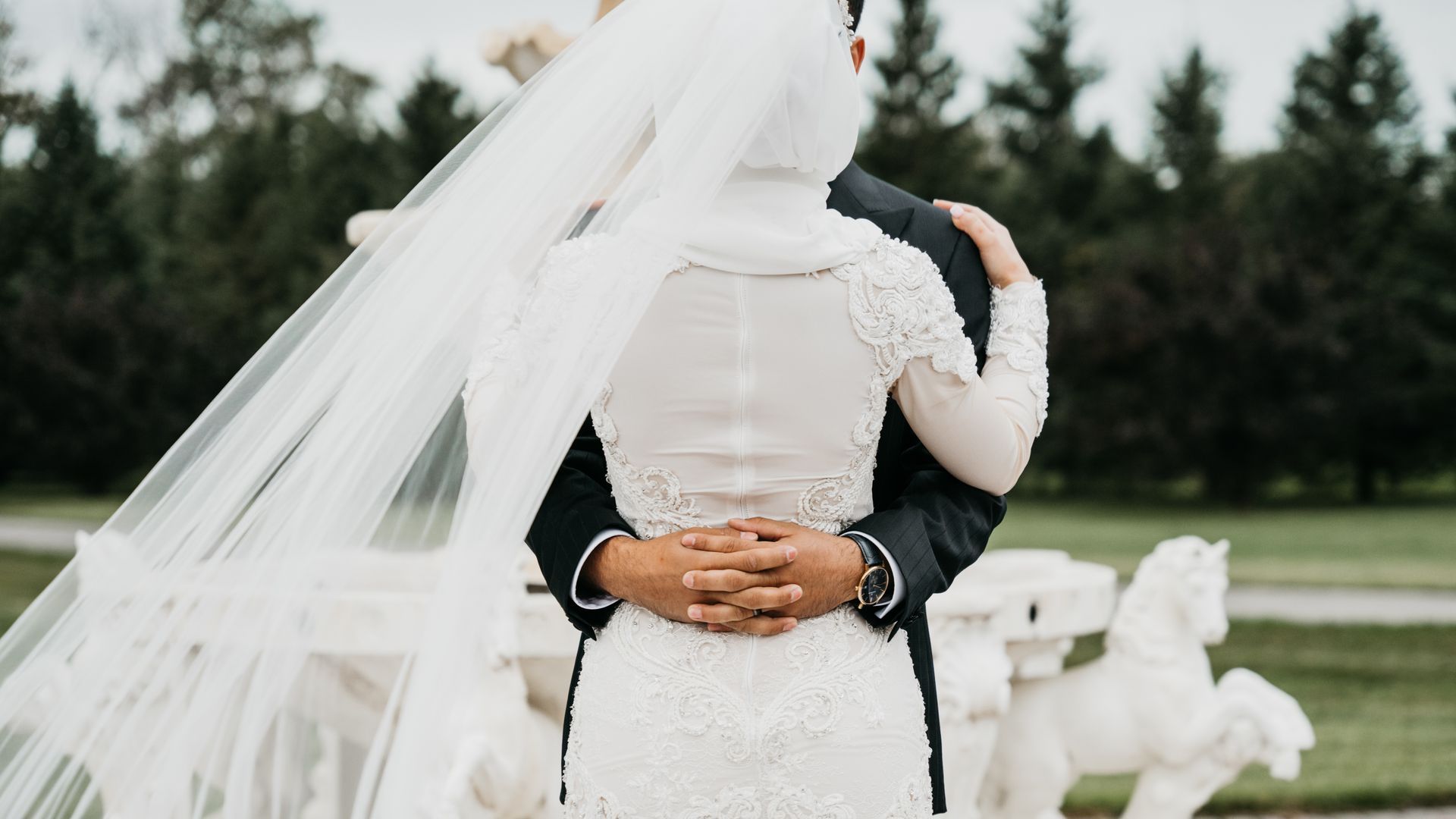 A bride and groom are hugging each other in front of a horse statue.