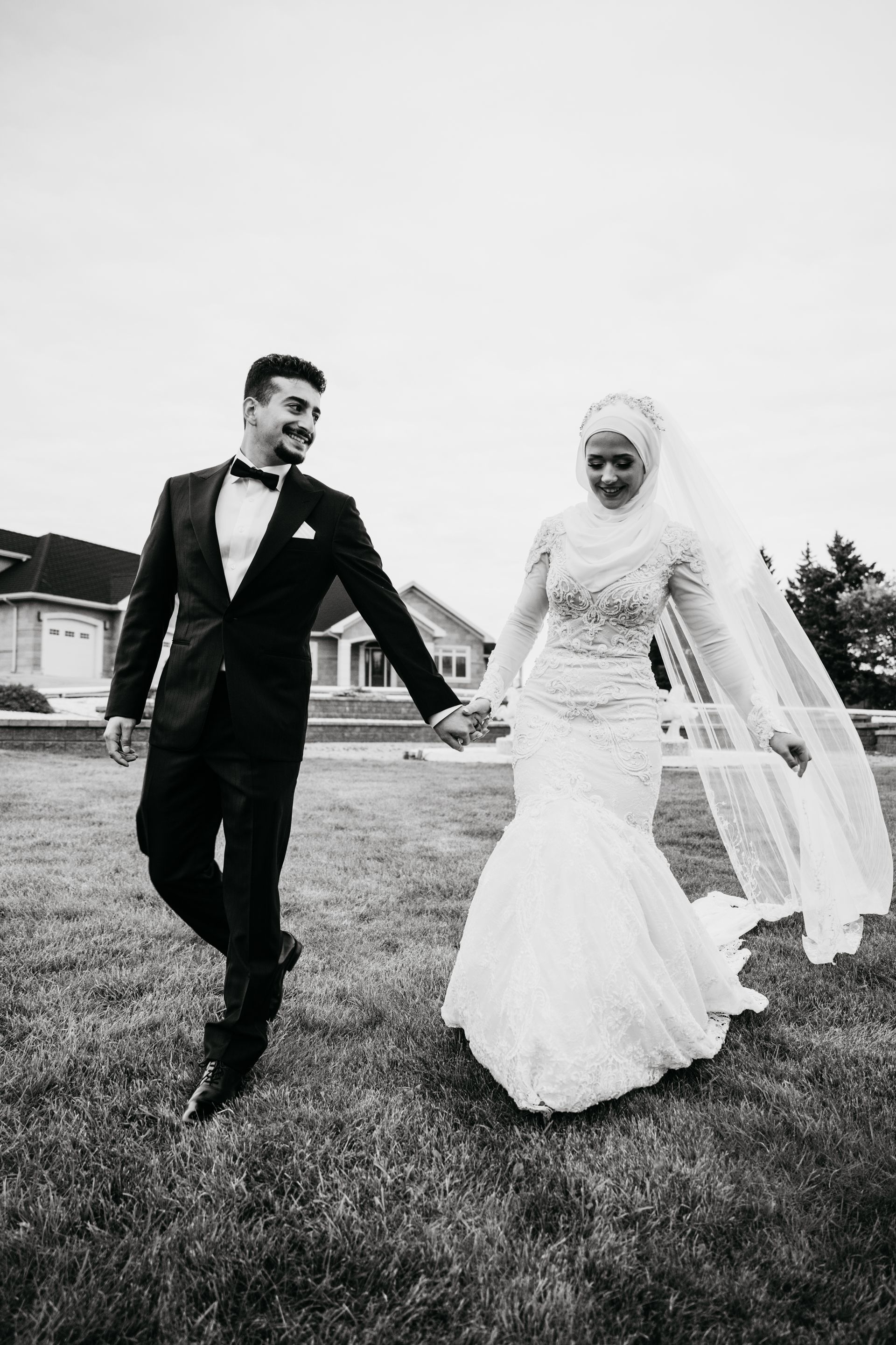 A black and white photo of a bride and groom holding hands.