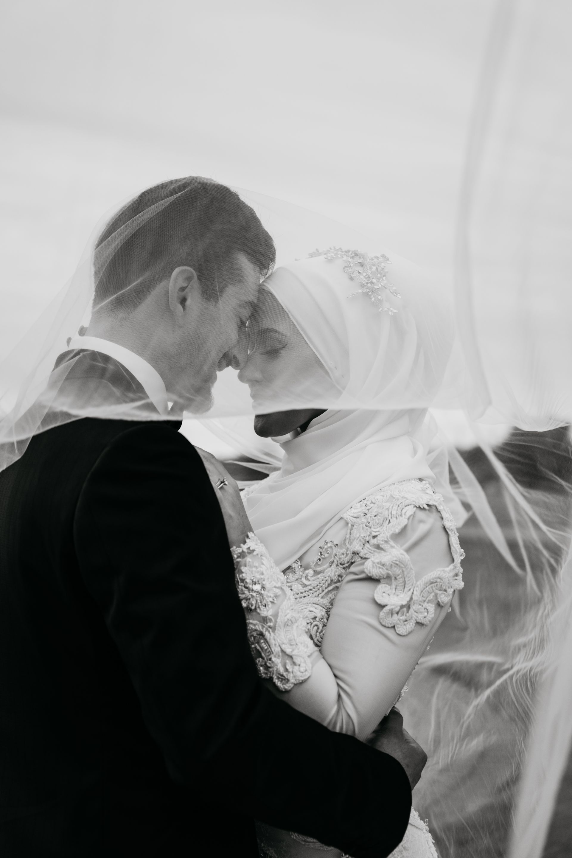 A bride and groom are kissing under a veil.
