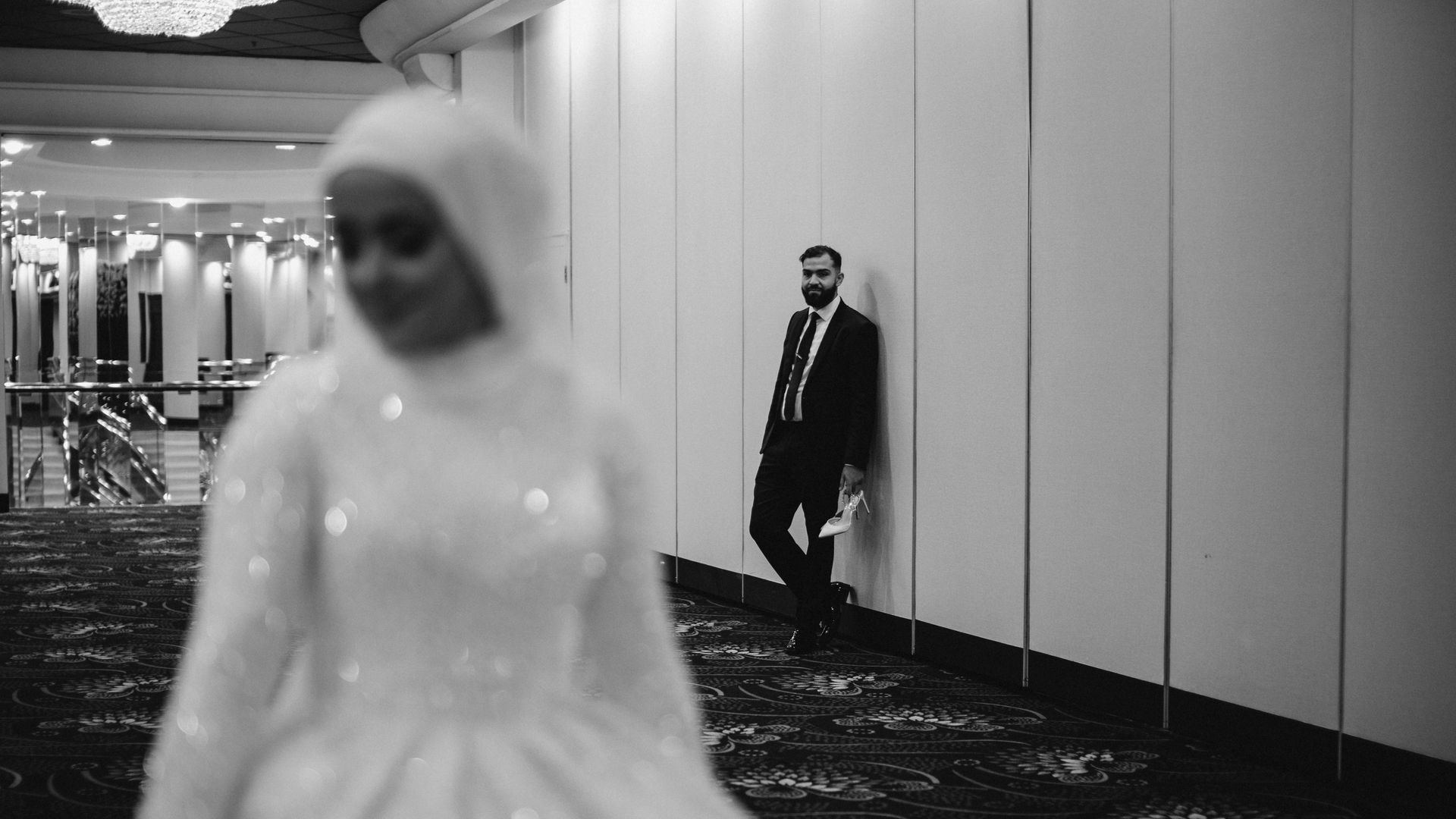 A black and white photo of a bride and groom leaning against a wall.