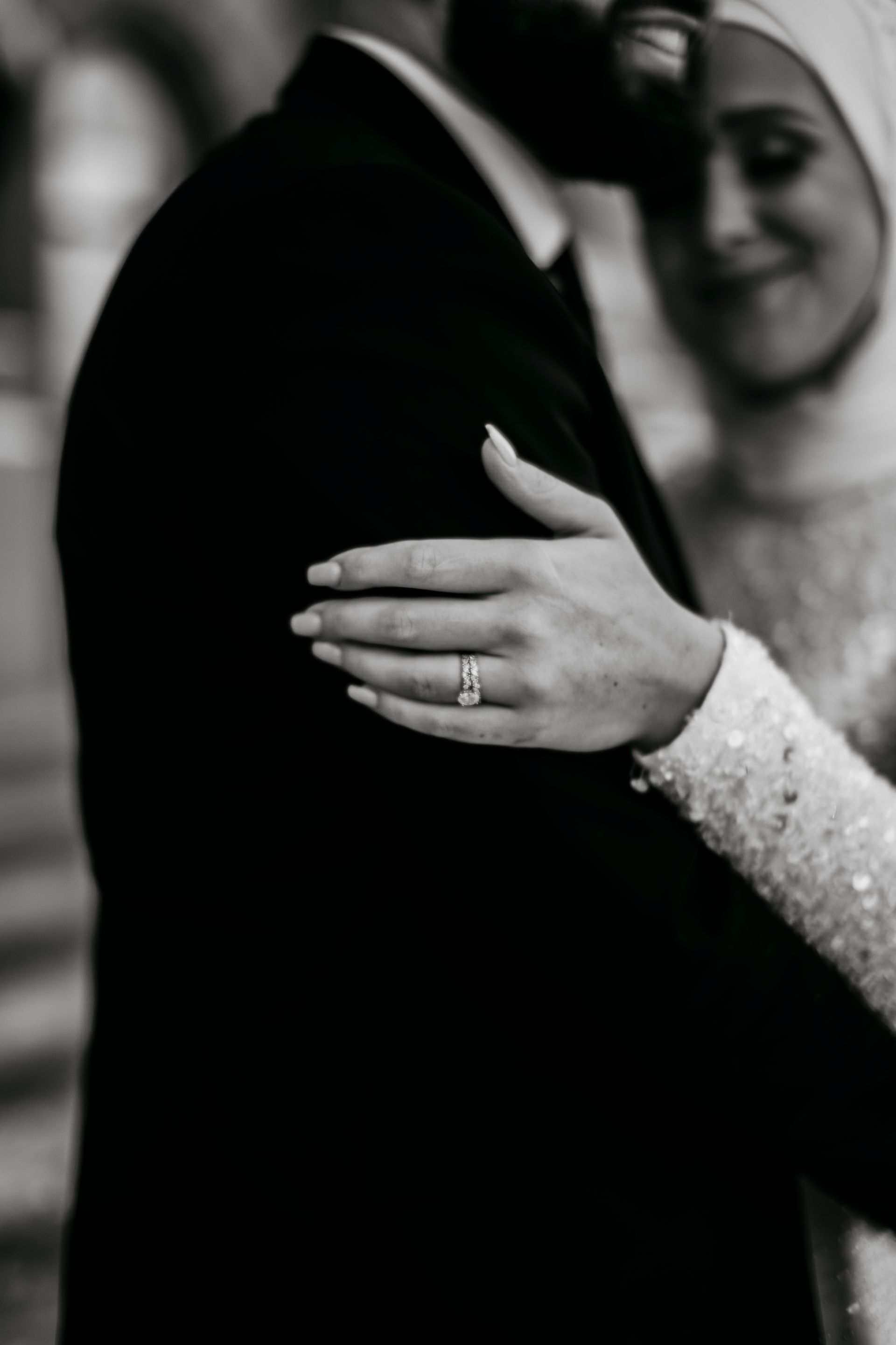 A black and white photo of a bride and groom hugging each other . the bride is wearing a wedding ring.