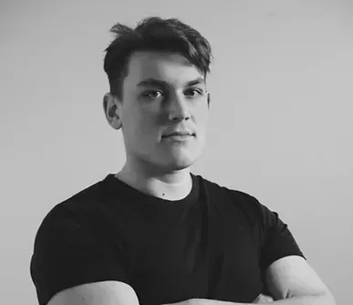 A young man in a black shirt is standing with his arms crossed.