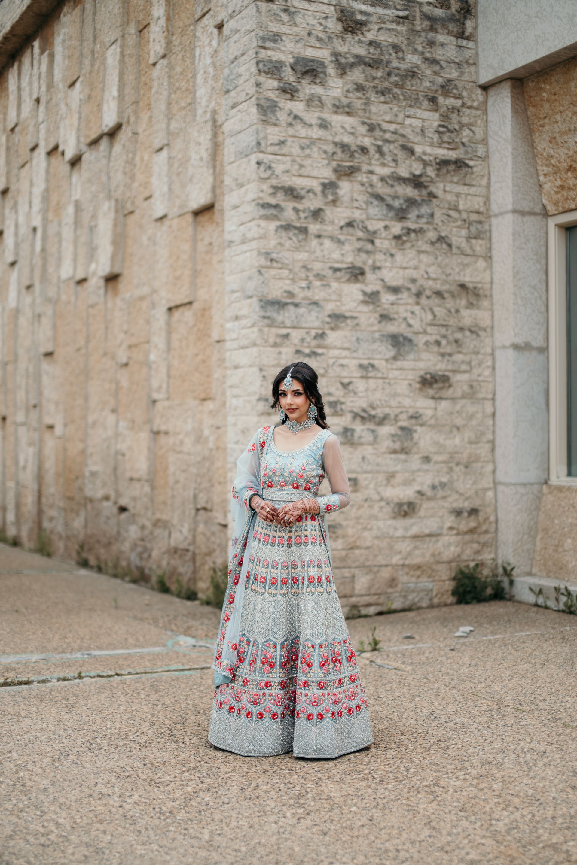 A woman in a long white dress is standing in front of a brick wall.