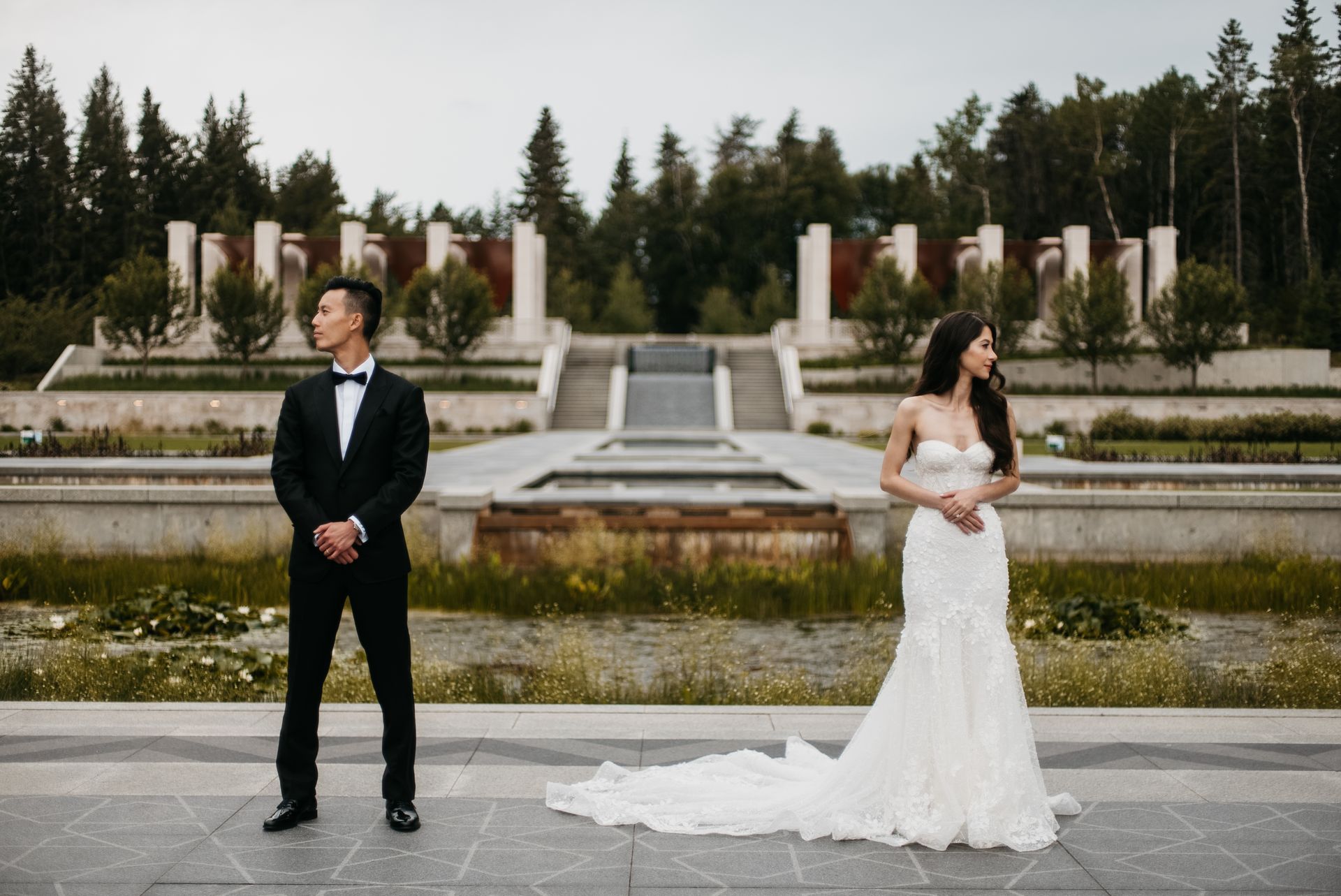 A bride and groom are standing next to each other in front of a fountain.