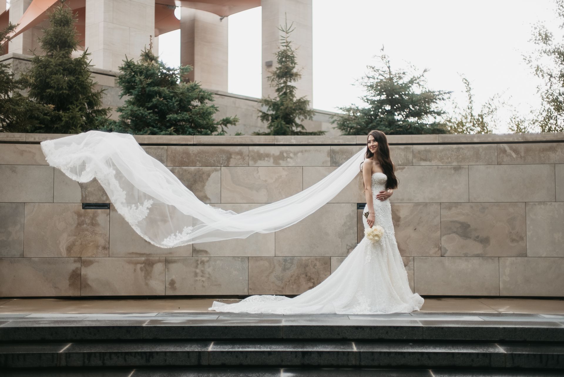 A bride in a wedding dress with a long veil blowing in the wind.