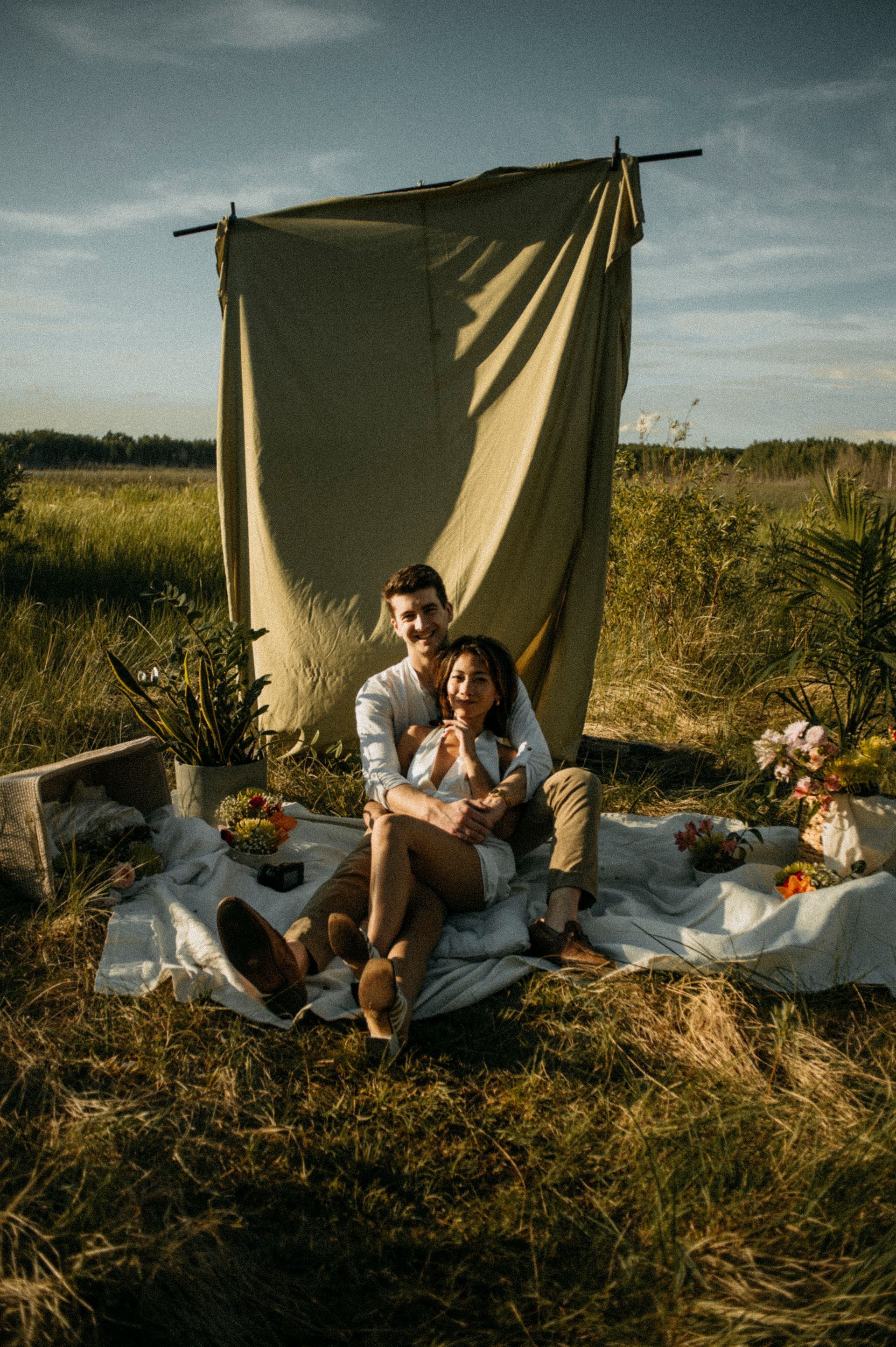 A man and a woman are sitting on a blanket in a field.