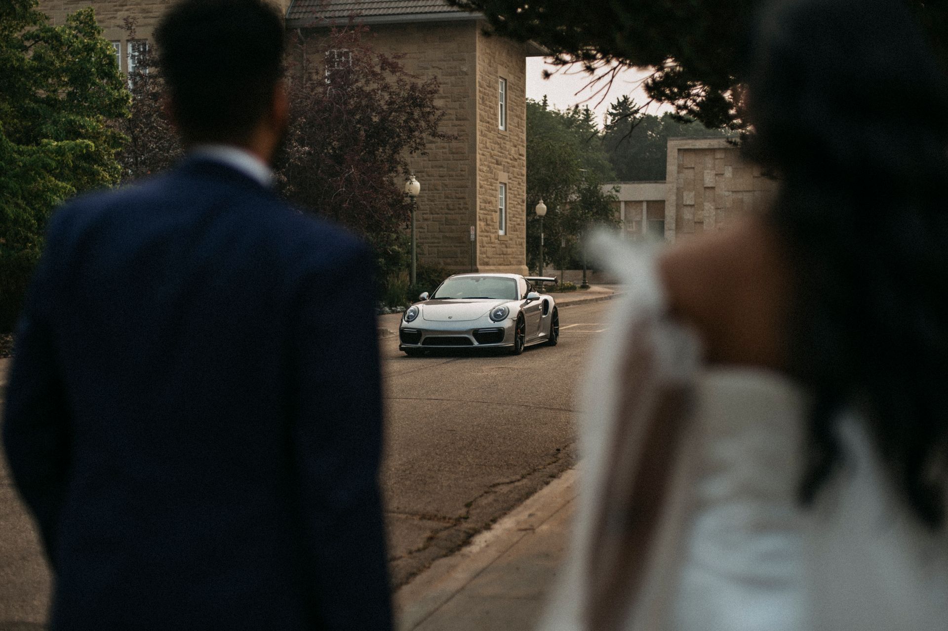 A bride and groom are standing in front of a white sports car.