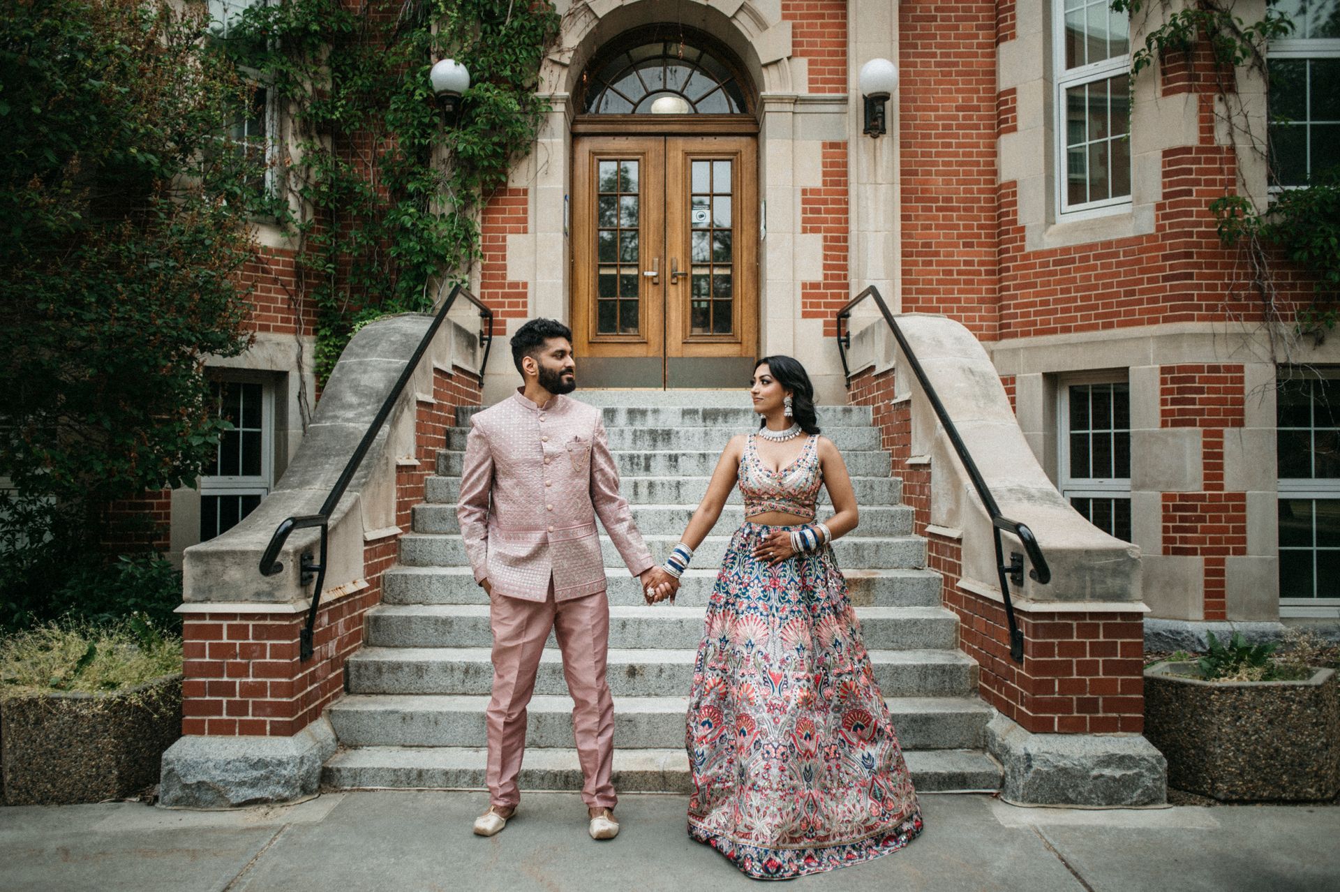 A man and a woman are standing on the steps of a building holding hands.