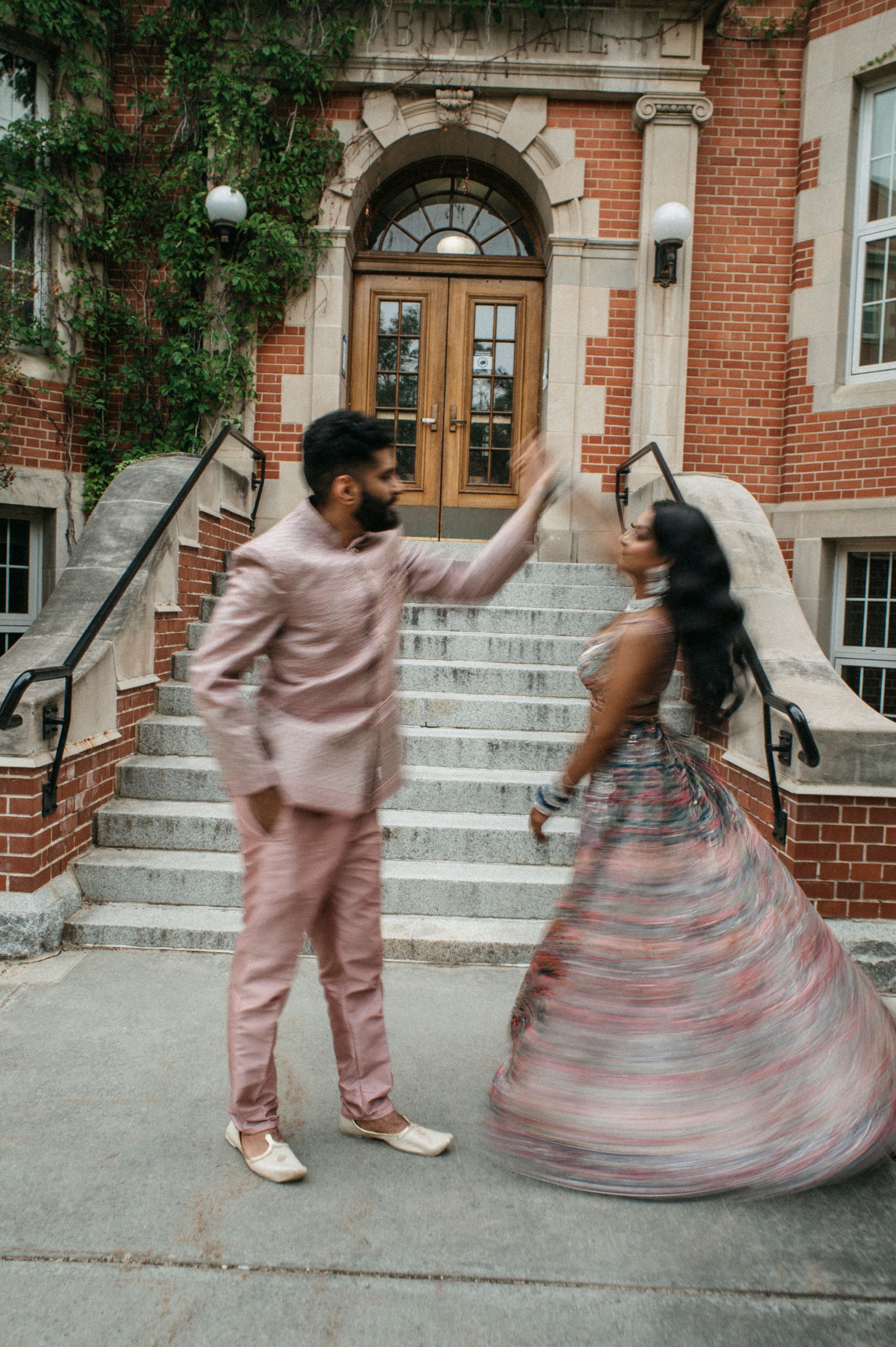 A bride and groom are dancing in front of a brick building.