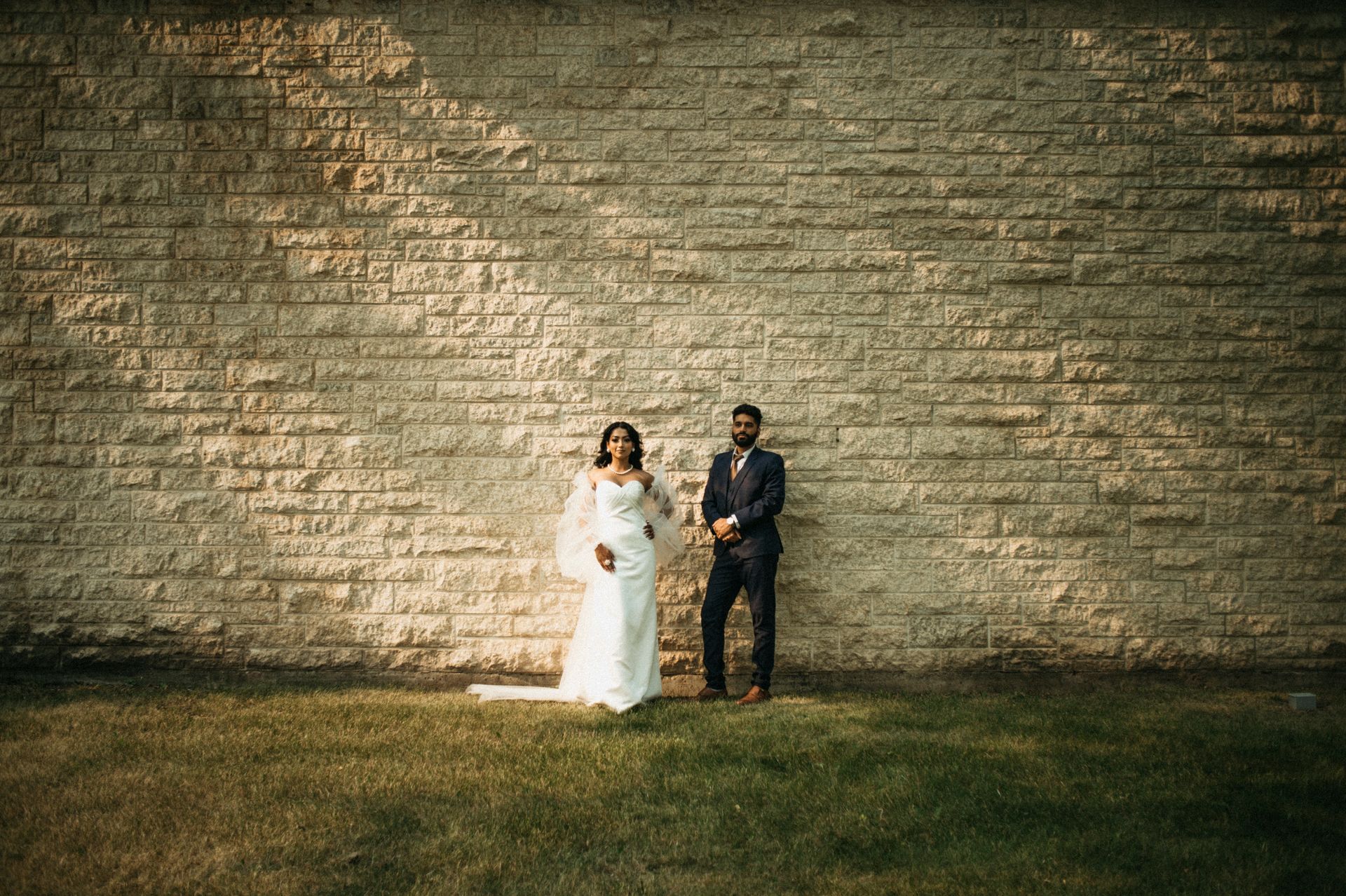 A bride and groom are standing in front of a brick wall.
