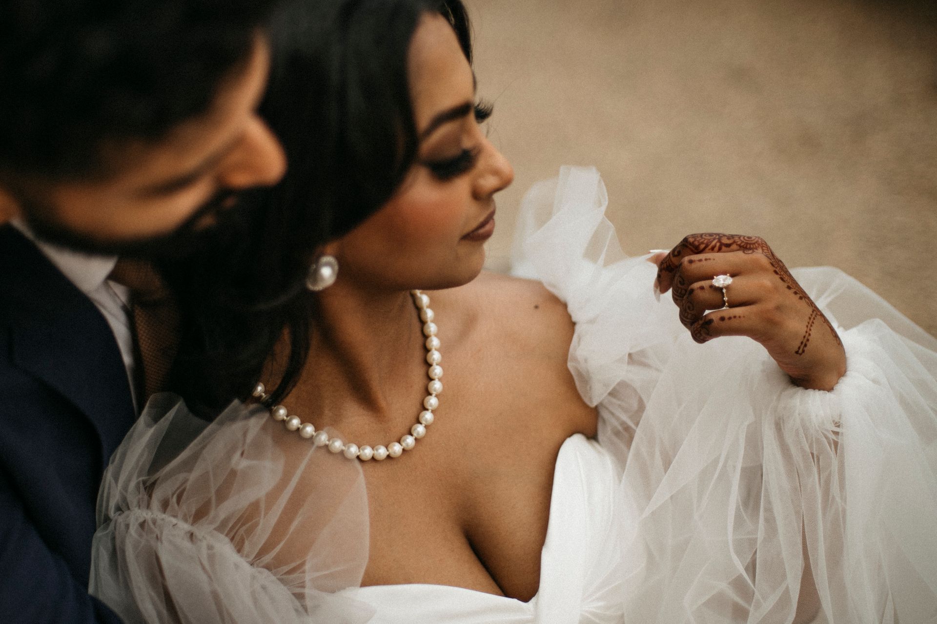 A bride and groom are posing for a picture while the bride is wearing a pearl necklace.