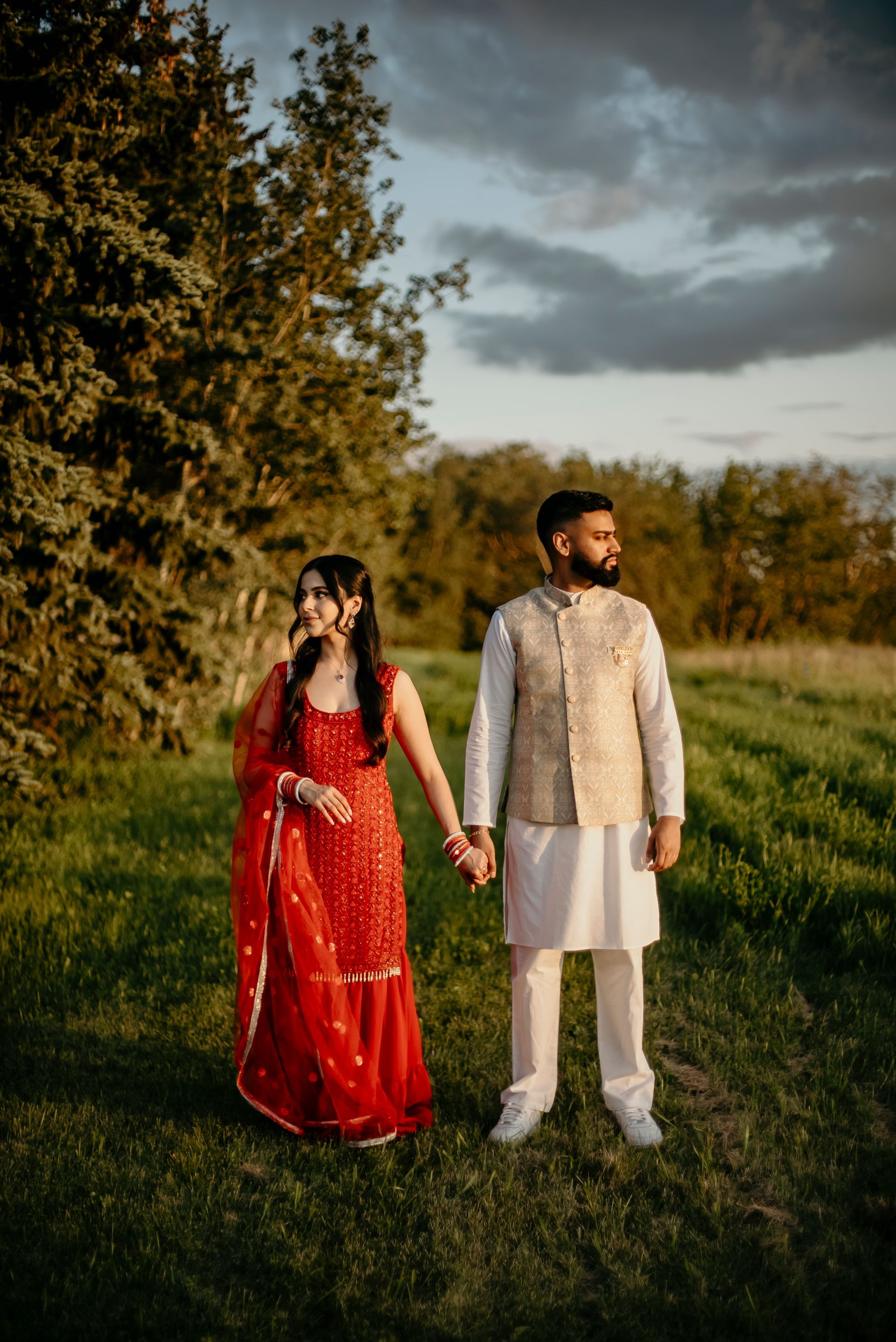 A man and a woman are standing in a field holding hands.