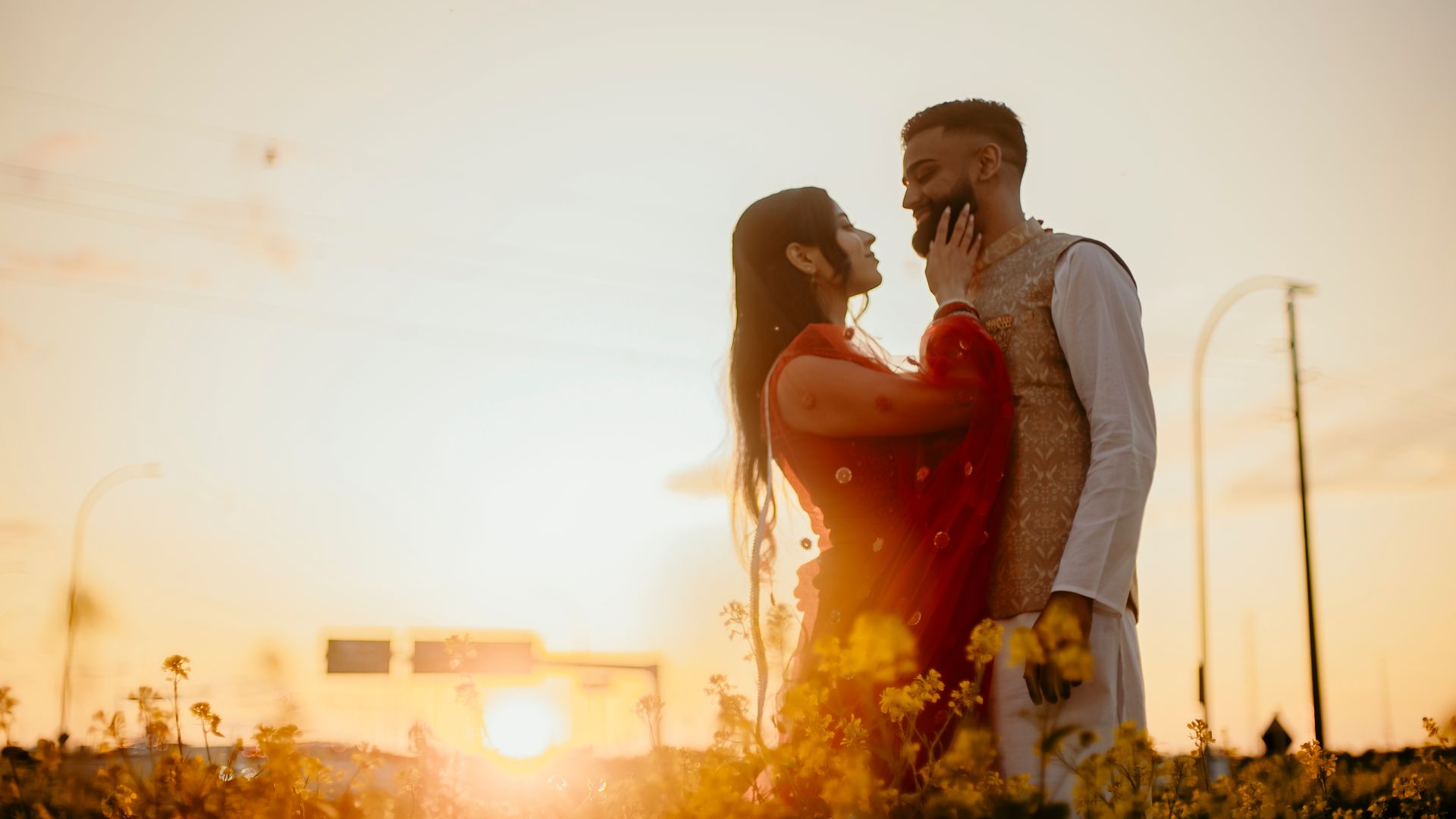 A man and a woman are kissing in a field of flowers at sunset.