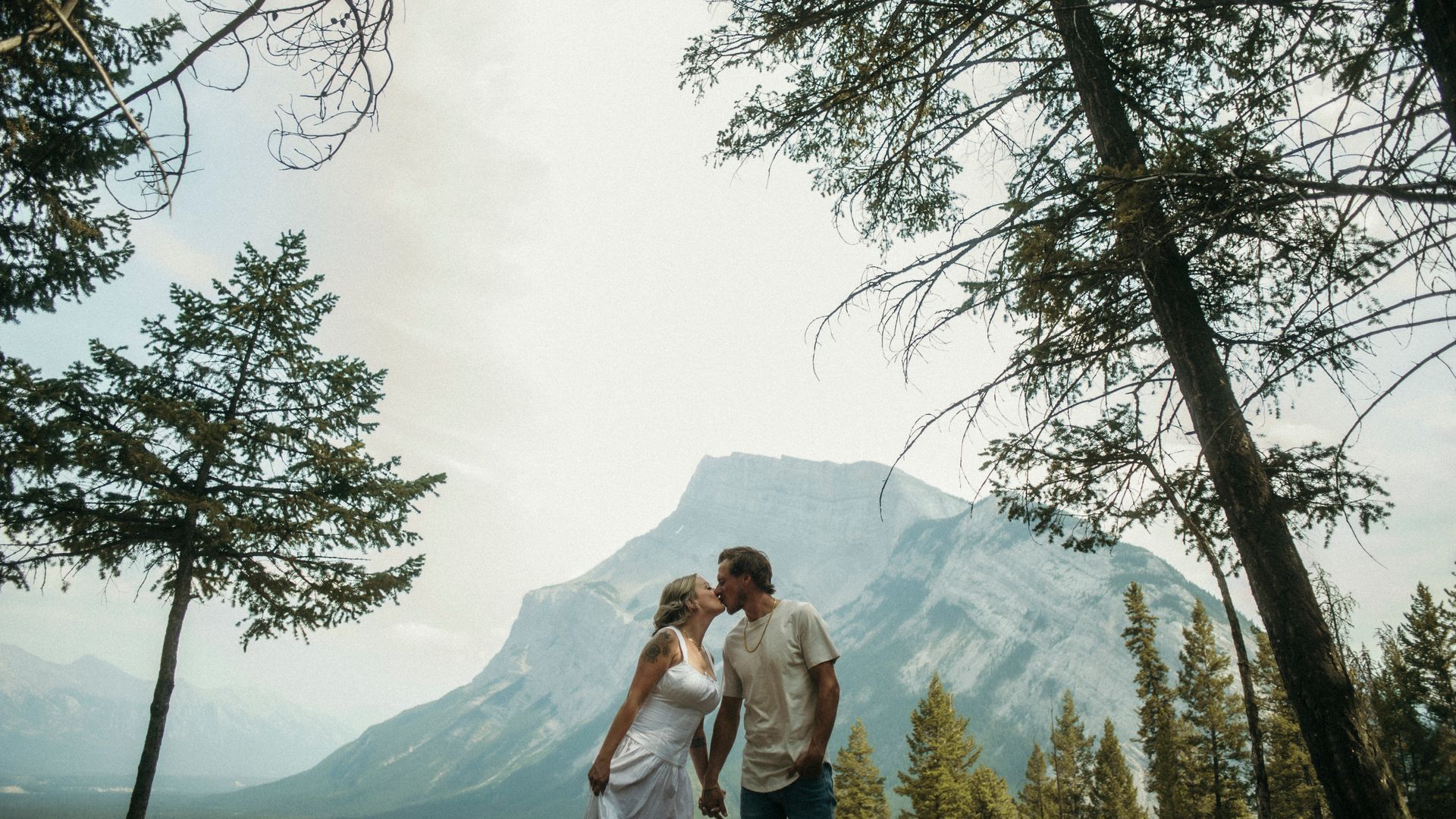 A man and a woman are kissing in front of a mountain.