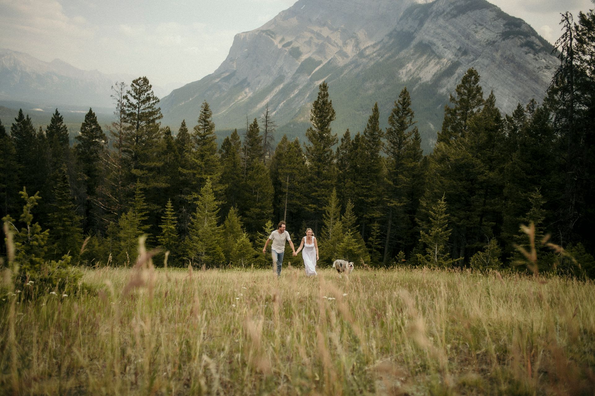 A man and woman are holding hands in a field with mountains in the background.