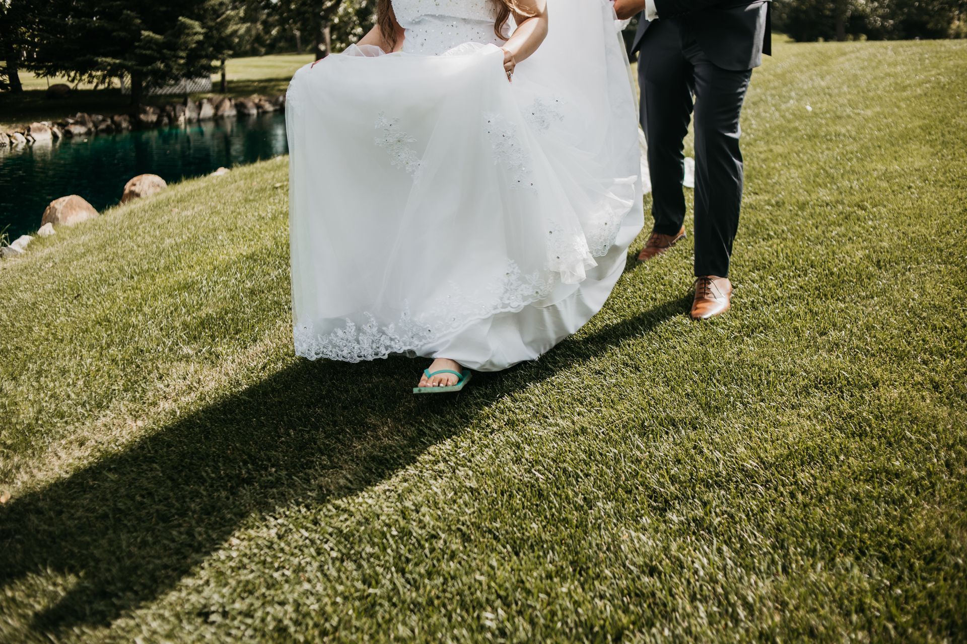 A bride and groom are walking through a grassy field.