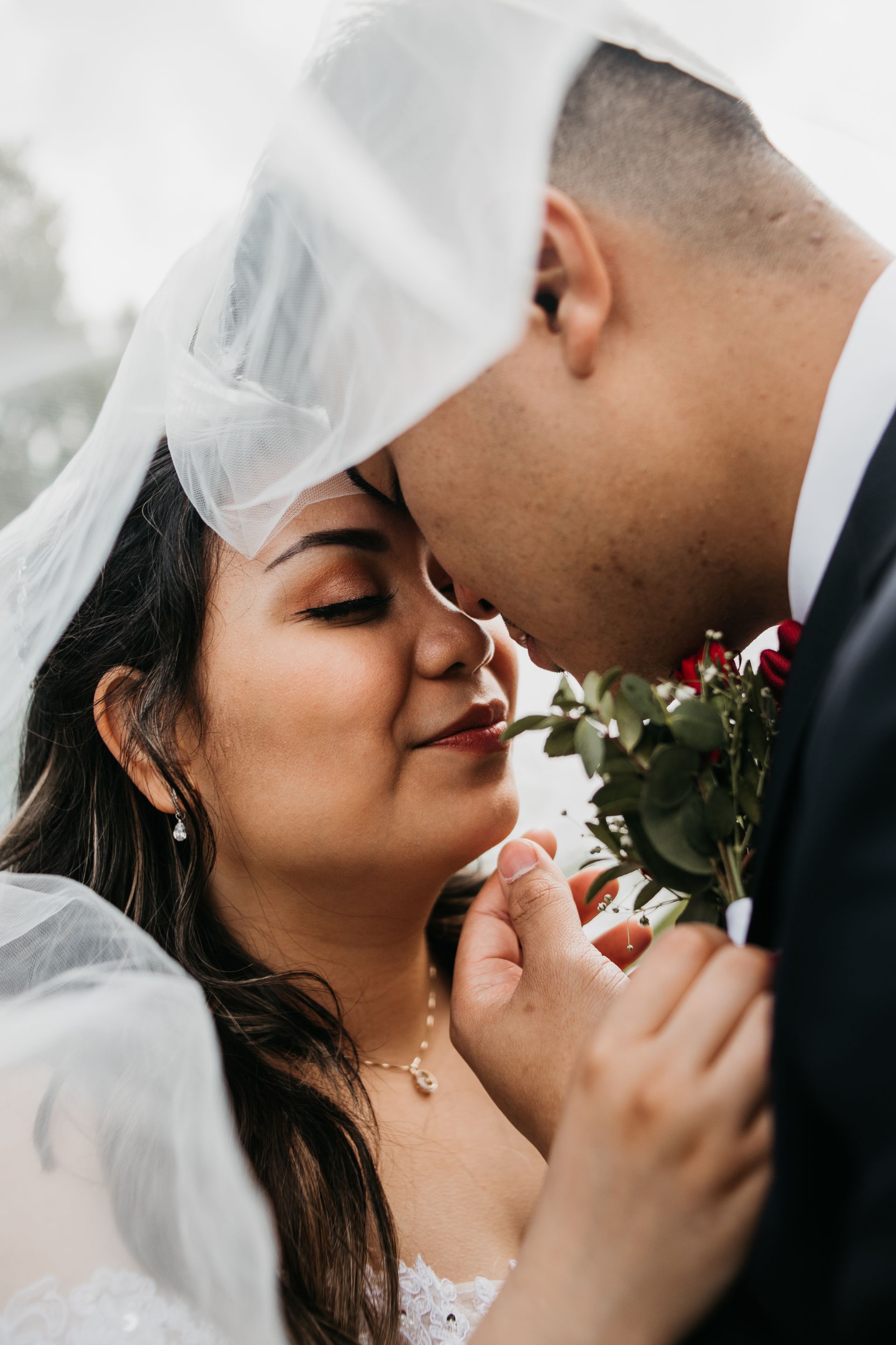 A bride and groom are kissing under a veil.