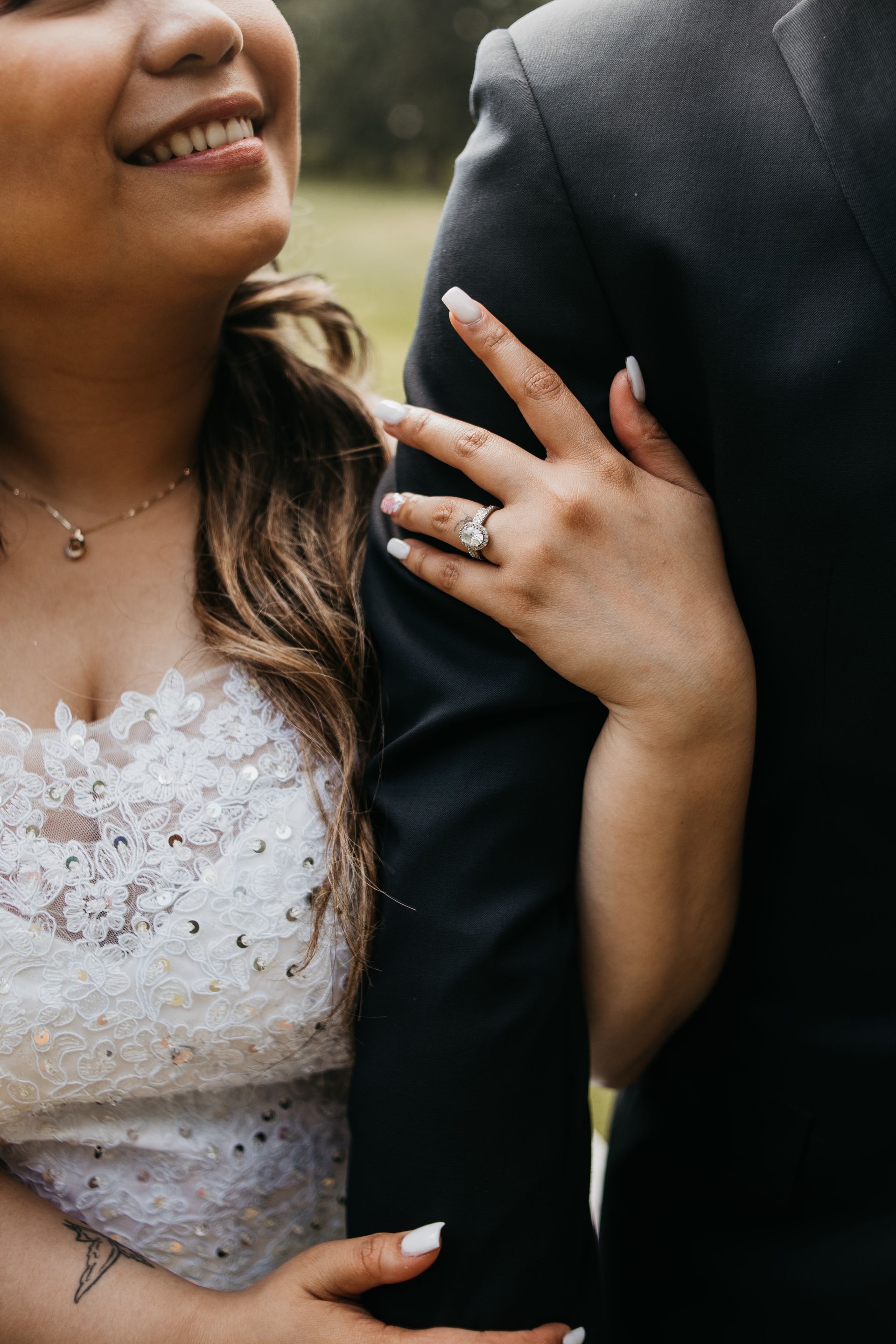 A bride and groom are posing for a picture and the bride is wearing a wedding ring.