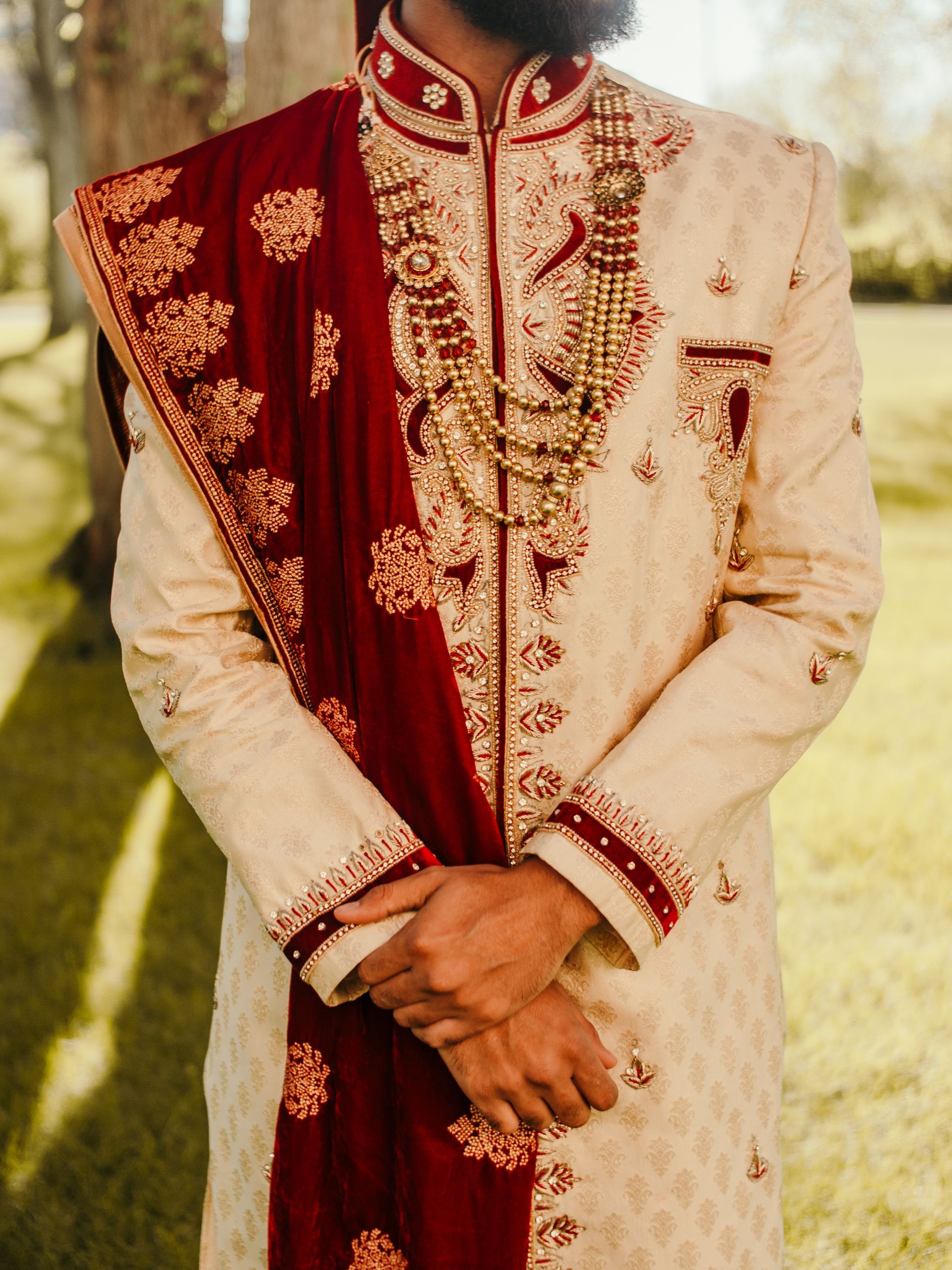 A man in a white and red dress is standing in the grass with his hands folded.