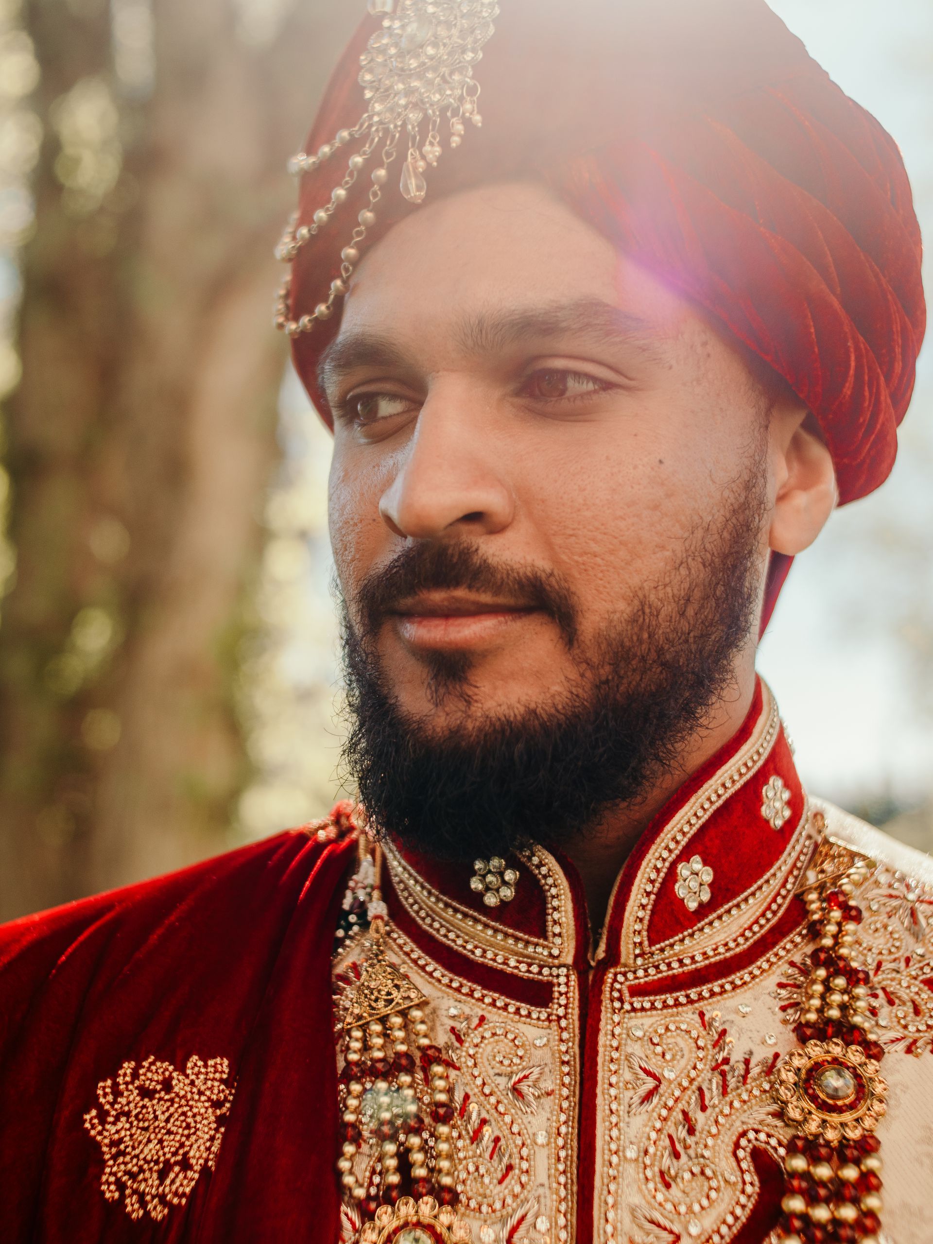 A man with a beard is wearing a red turban and a red jacket.