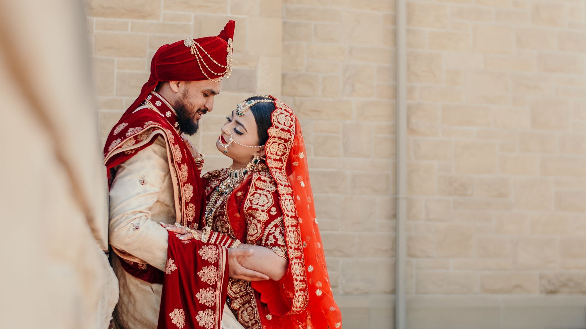 A bride and groom are standing next to each other in front of a brick wall.