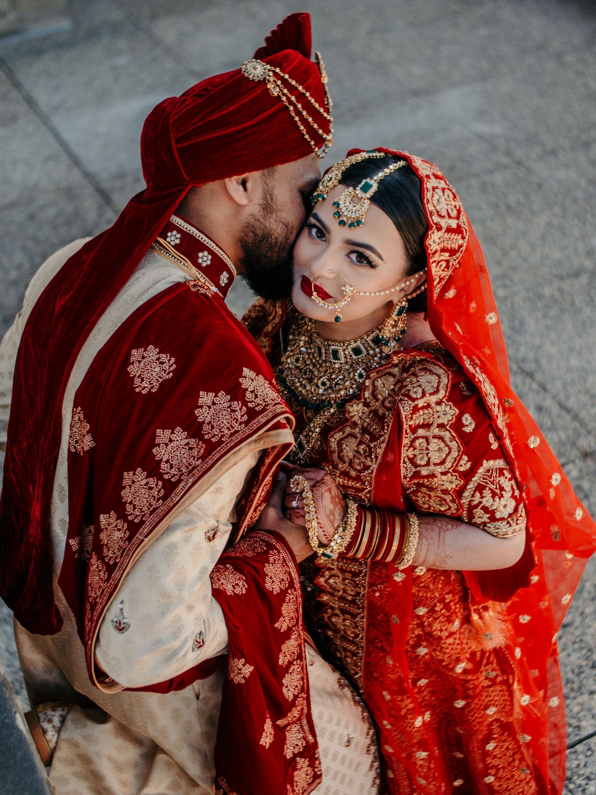 A bride and groom are posing for a picture while the bride is kissing the groom on the cheek.