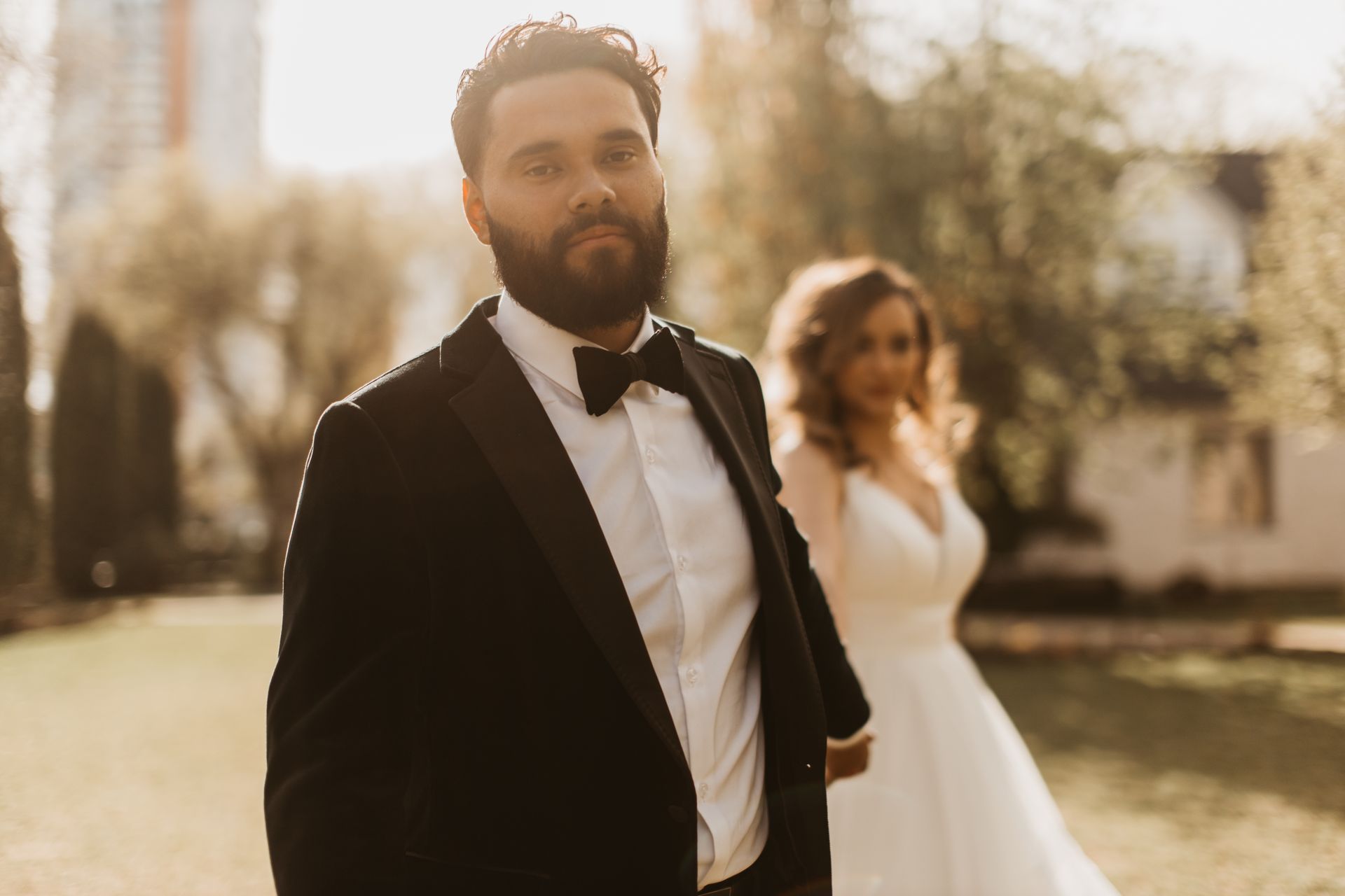 A bearded man in a tuxedo and bow tie is standing next to a bride in a white dress.