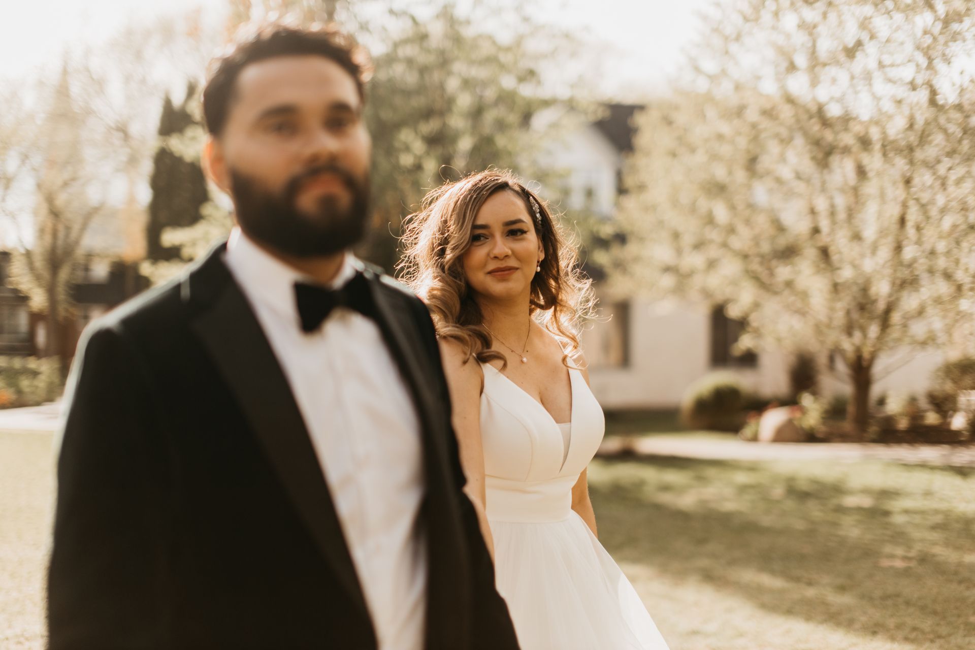 A bride and groom are standing next to each other in a park.