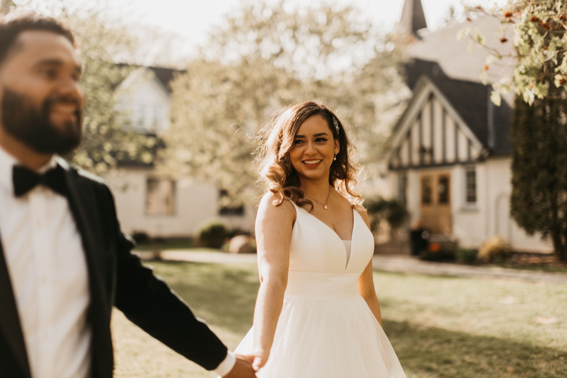 A bride and groom are holding hands in front of a white house.