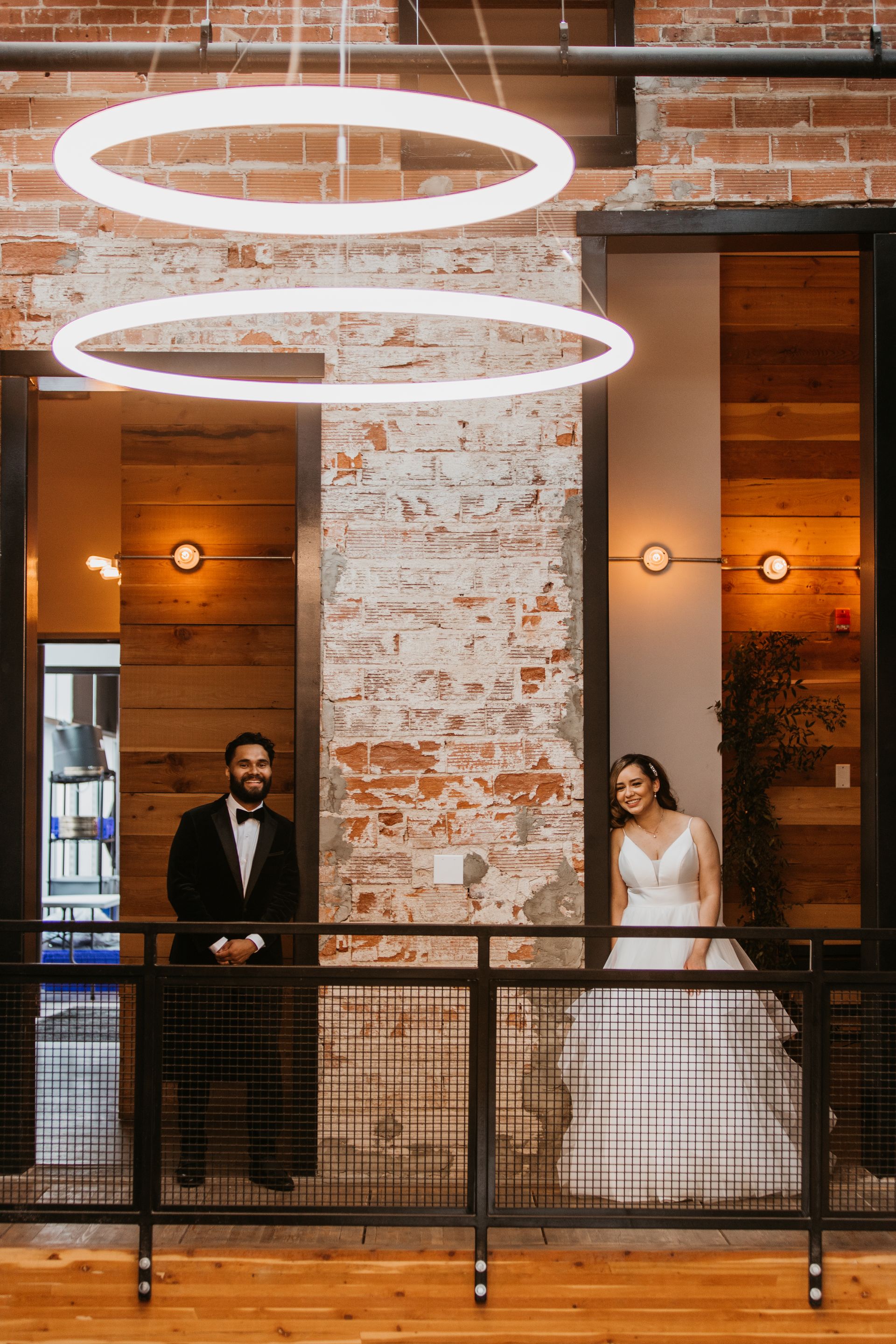 A bride and groom are standing on a balcony in front of a brick wall.