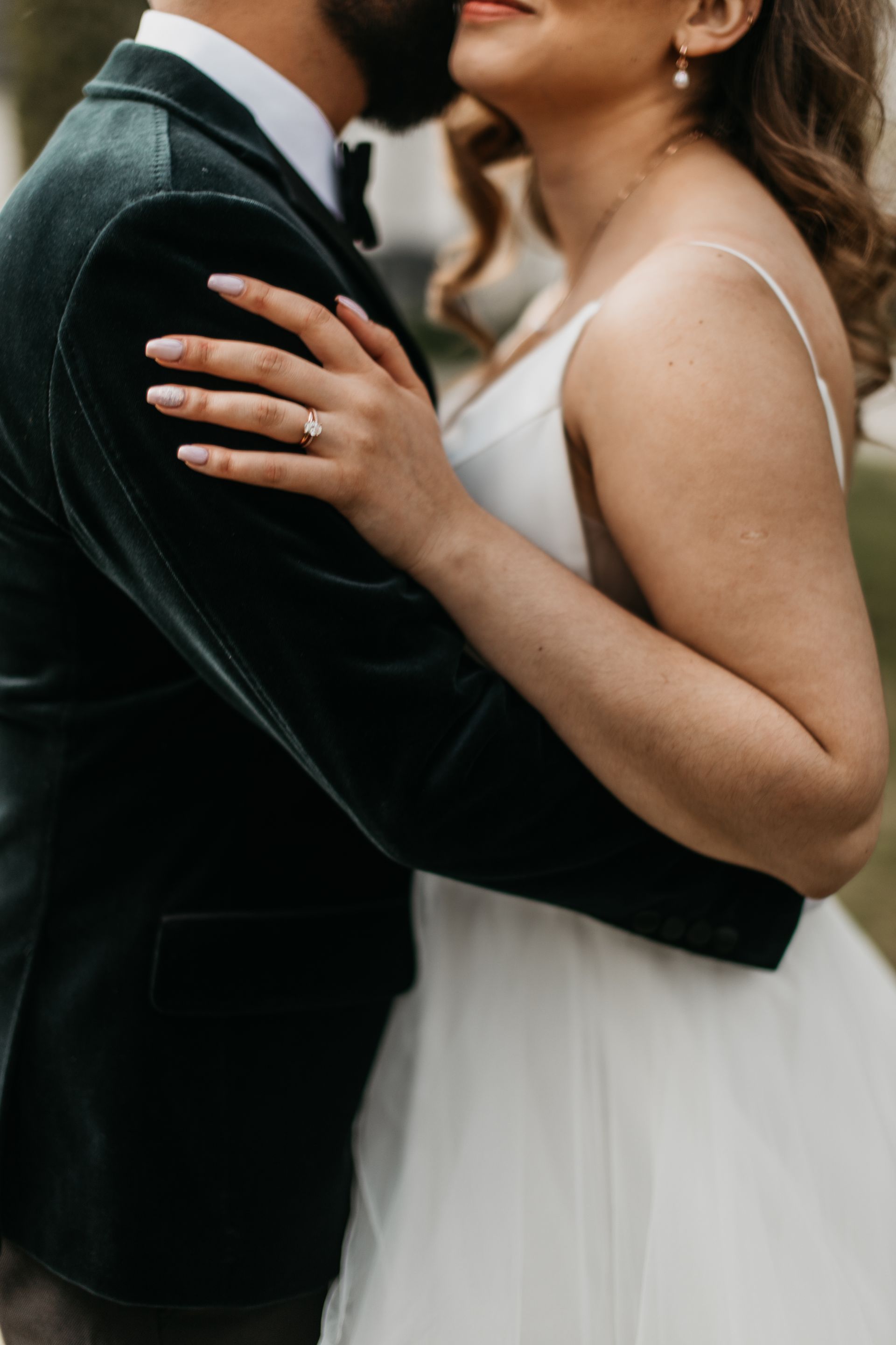 A bride and groom are hugging each other and the bride is wearing a wedding ring.