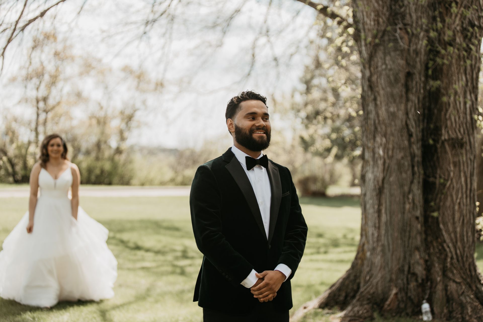 A bride and groom are standing next to each other in front of a tree.
