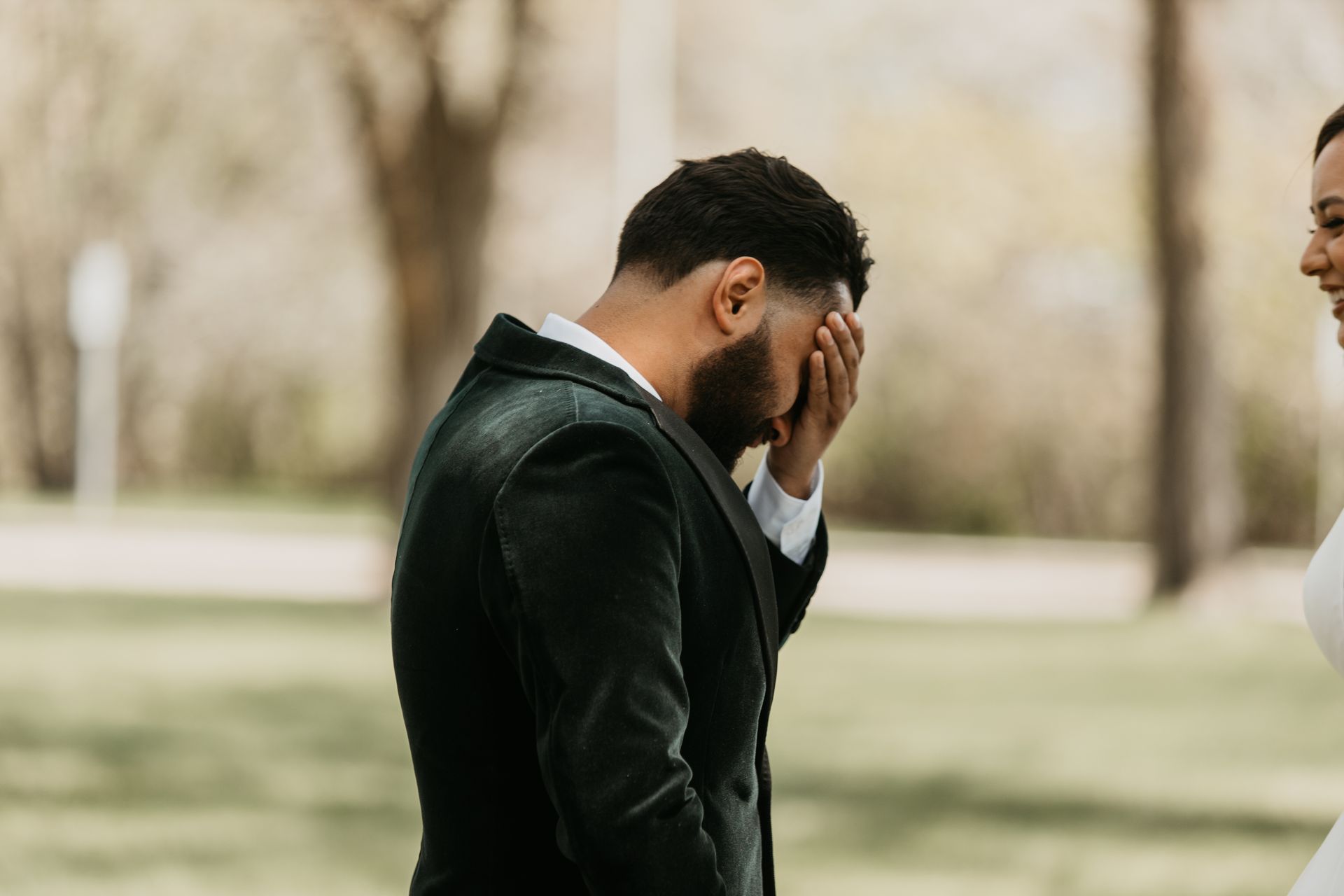A man in a suit is covering his face while standing next to a woman in a white dress.