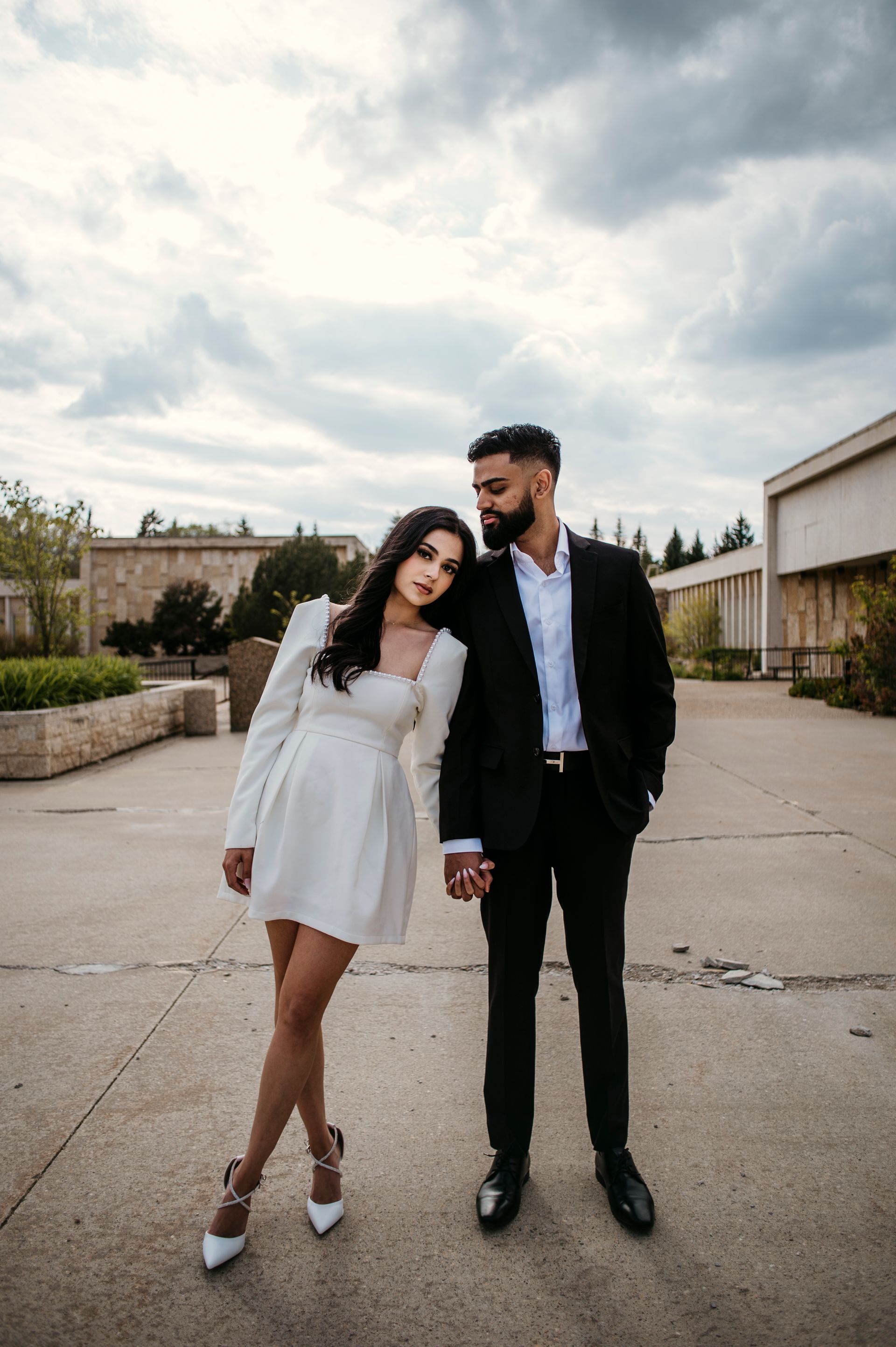 A man and a woman are standing next to each other on a sidewalk holding hands.