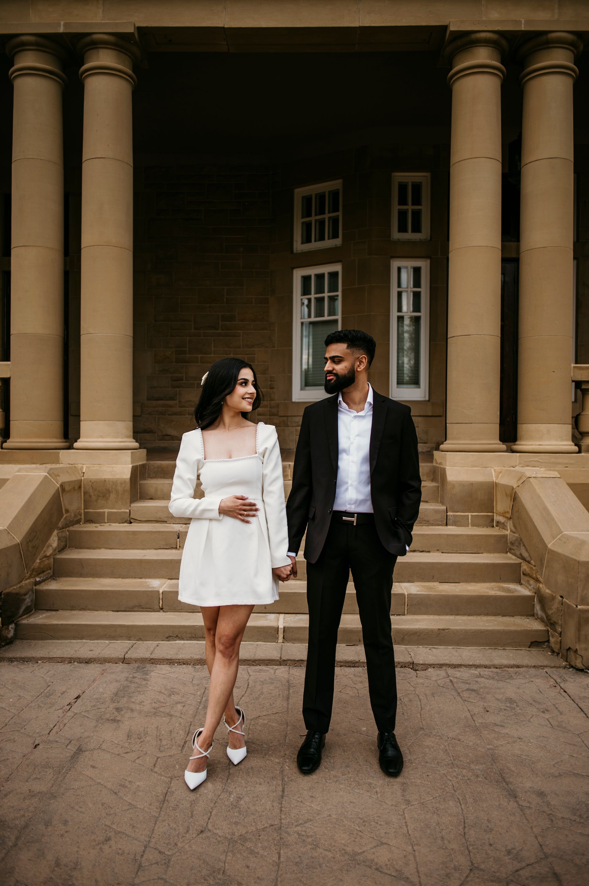 A man and a woman are standing in front of a building holding hands.