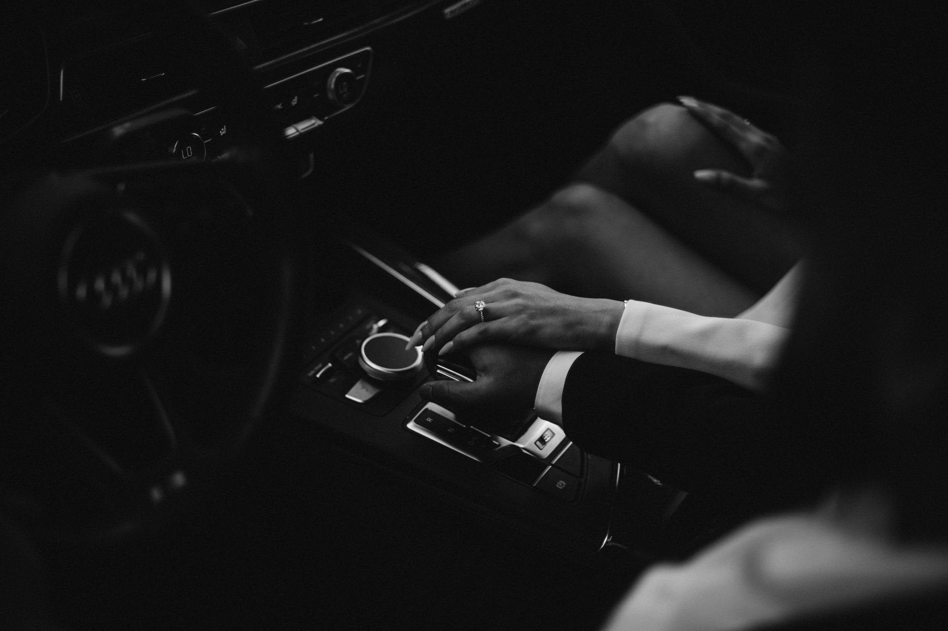 A black and white photo of a man and woman holding hands in a car.