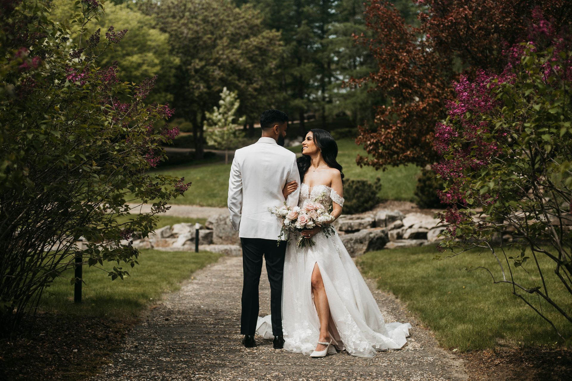 A bride and groom are walking down a path in a park.