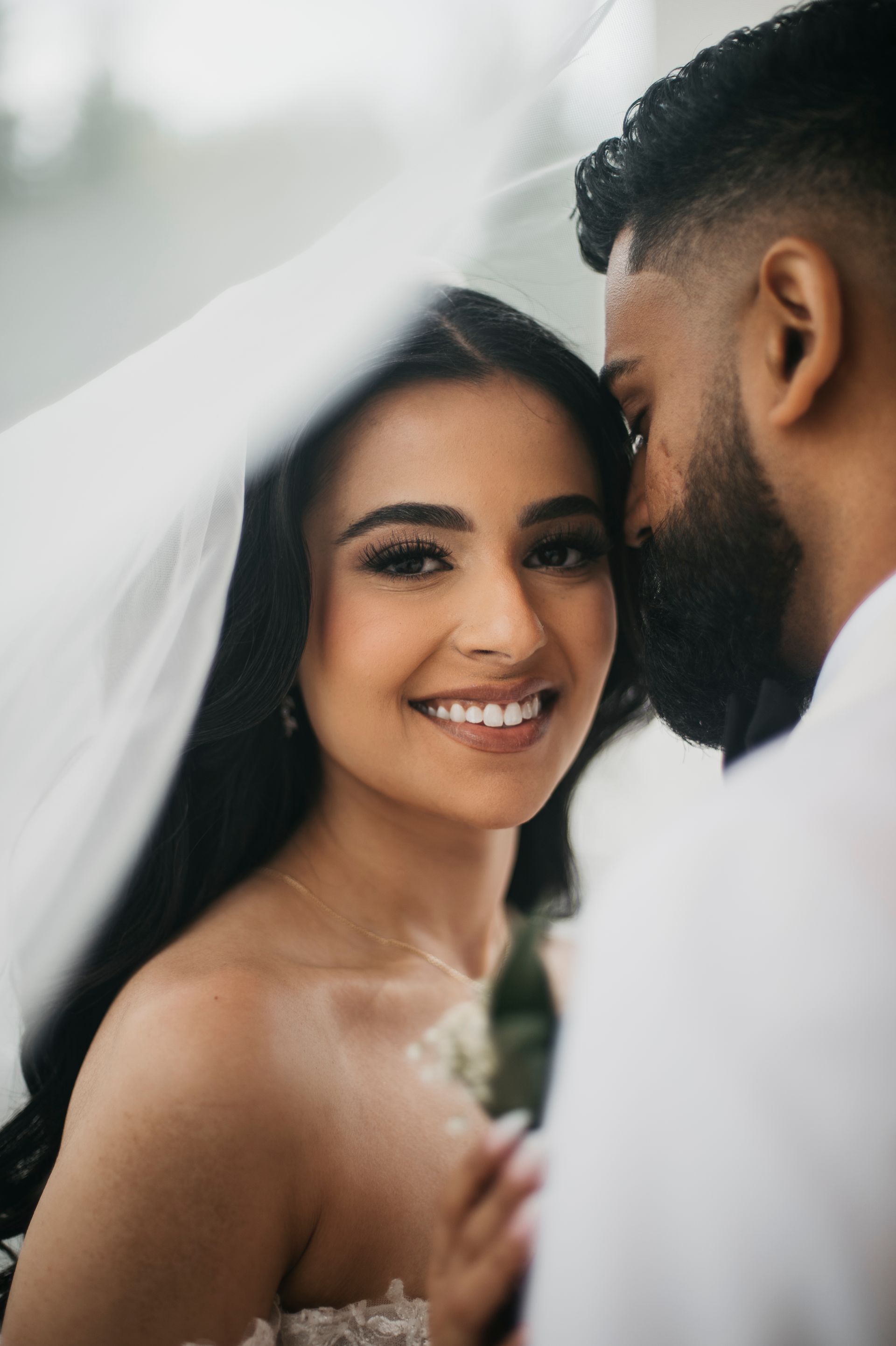 A bride and groom are posing for a picture under a veil.